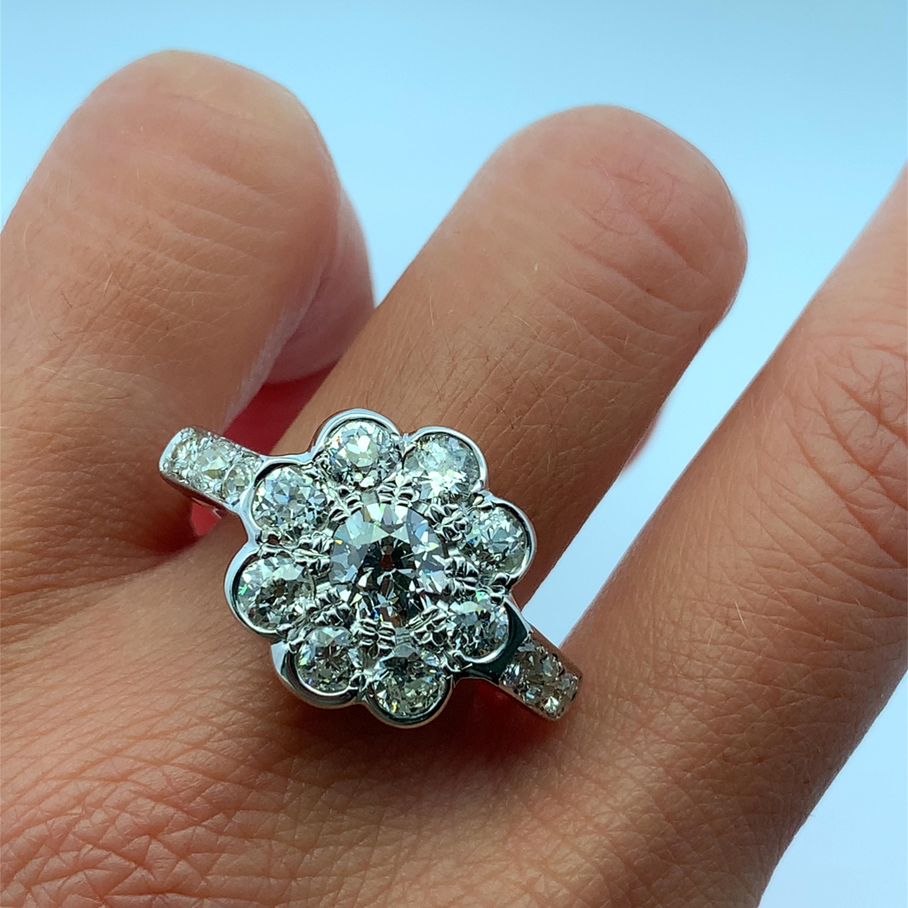 This stunning floral diamond ring features a captivating design that radiates elegance and charm. The central old cut diamond is surrounded by a halo cluster of smaller stones, creating a beautiful bloom effect that is perfect for any occasion.