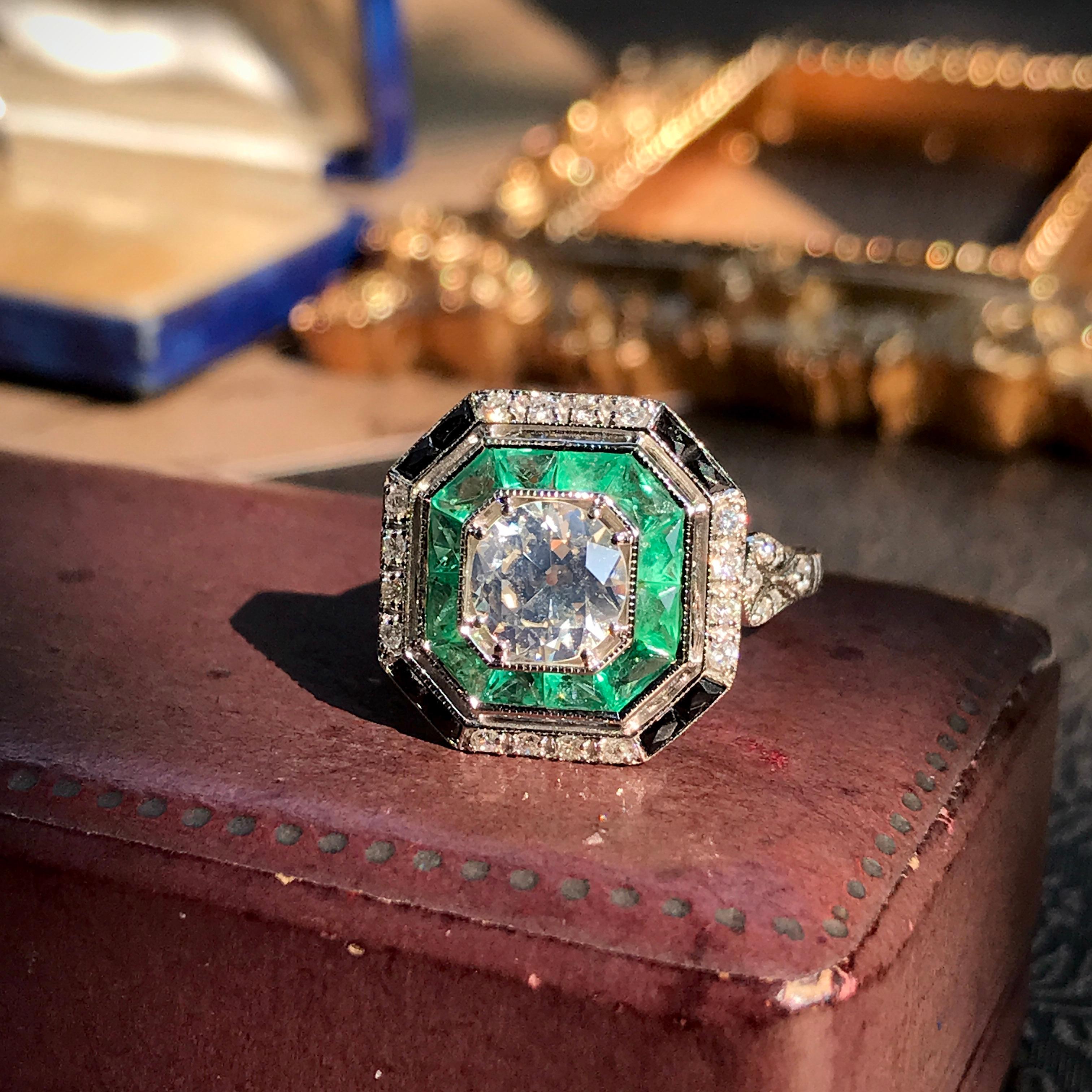An 18k white gold Art-Deco design diamond emerald and onyx target ring, center diamond with an outer ring of round diamonds an inner one of French cut emeralds and onyx and finished with millgrain edging, finished with diamond shoulders.

Ring