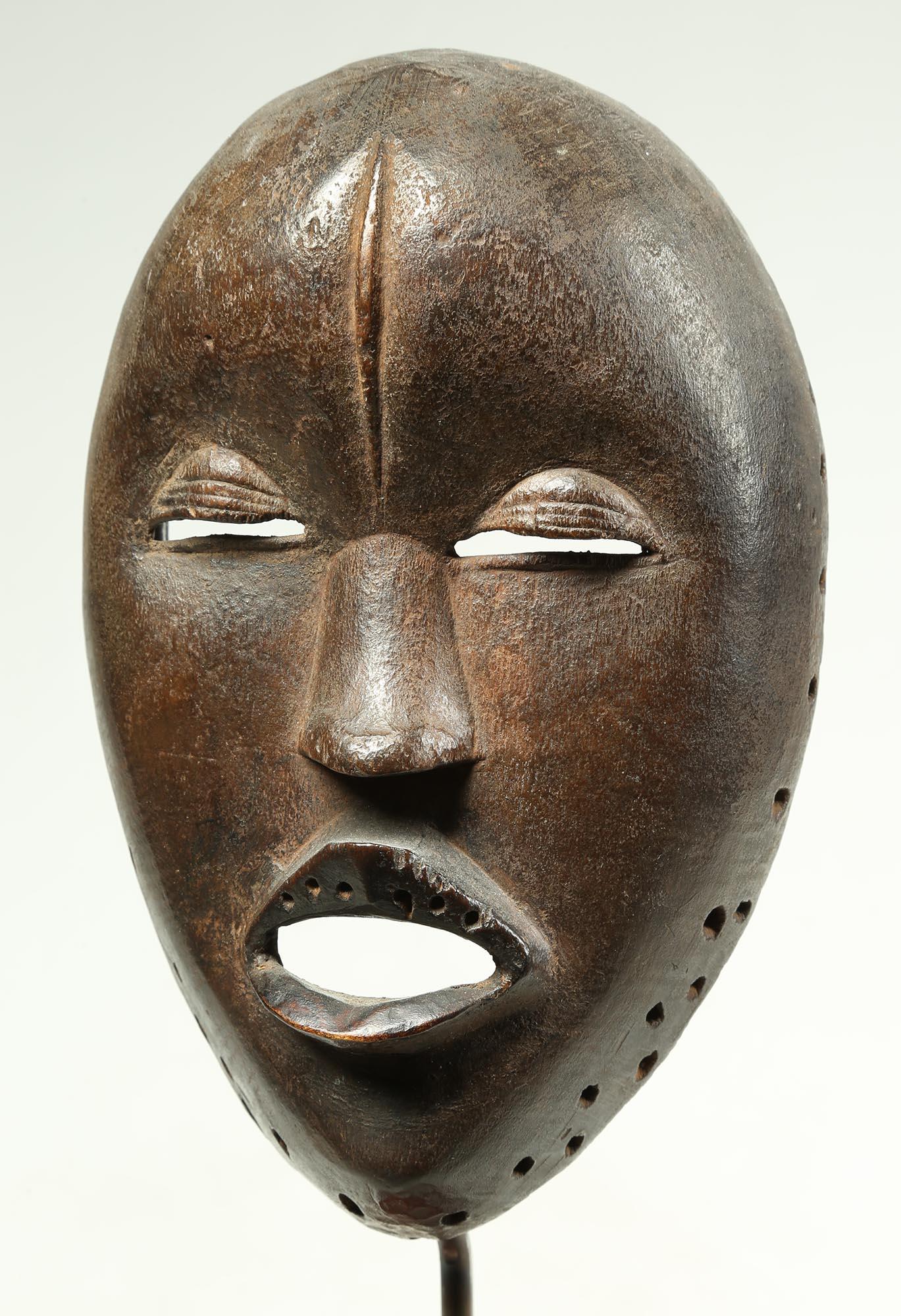 Old expressive Dan mask with open mouth as if speaking or singing, with heavy eyelids as if lost in a trance. Holes around mouth once held inserted teeth, now missing. Small holes around rim for attachment of dance costume. Created in the early 20th