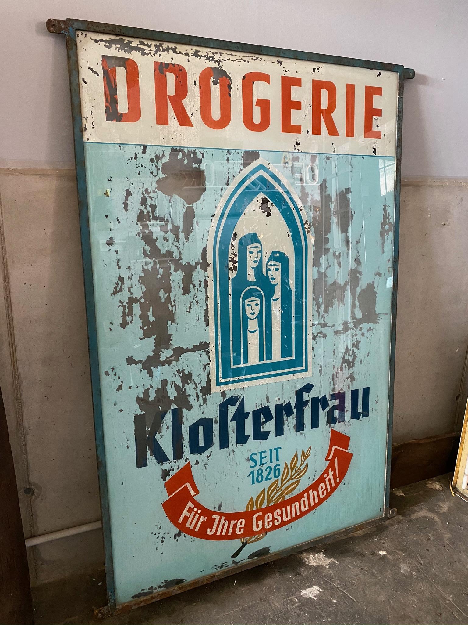 This old drugstore advertisement for Klosterfrau comes from a drugstore liquidation and is from the 1920s. The advertisement was painted behind glass, which is slowly peeling off. Framed in blue lacquered metal and provided with 4 eyelets for