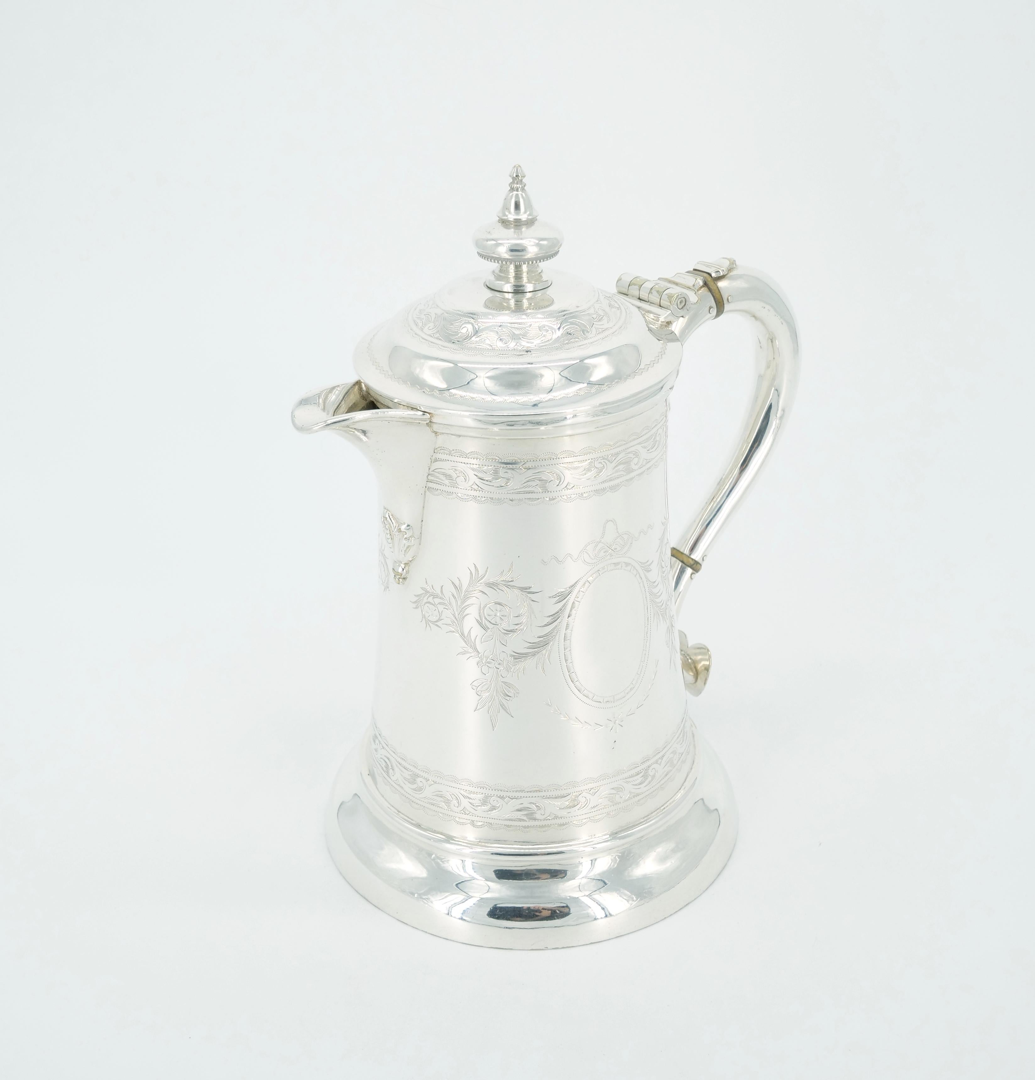 Elevate your collection with the exquisite charm of our Old English Silver Plate Queen Anne Tankard by Walker & Hall. The exterior boasts a rich silver plate finish adorned with finely engraved foliate decoration details on both sides, adding a