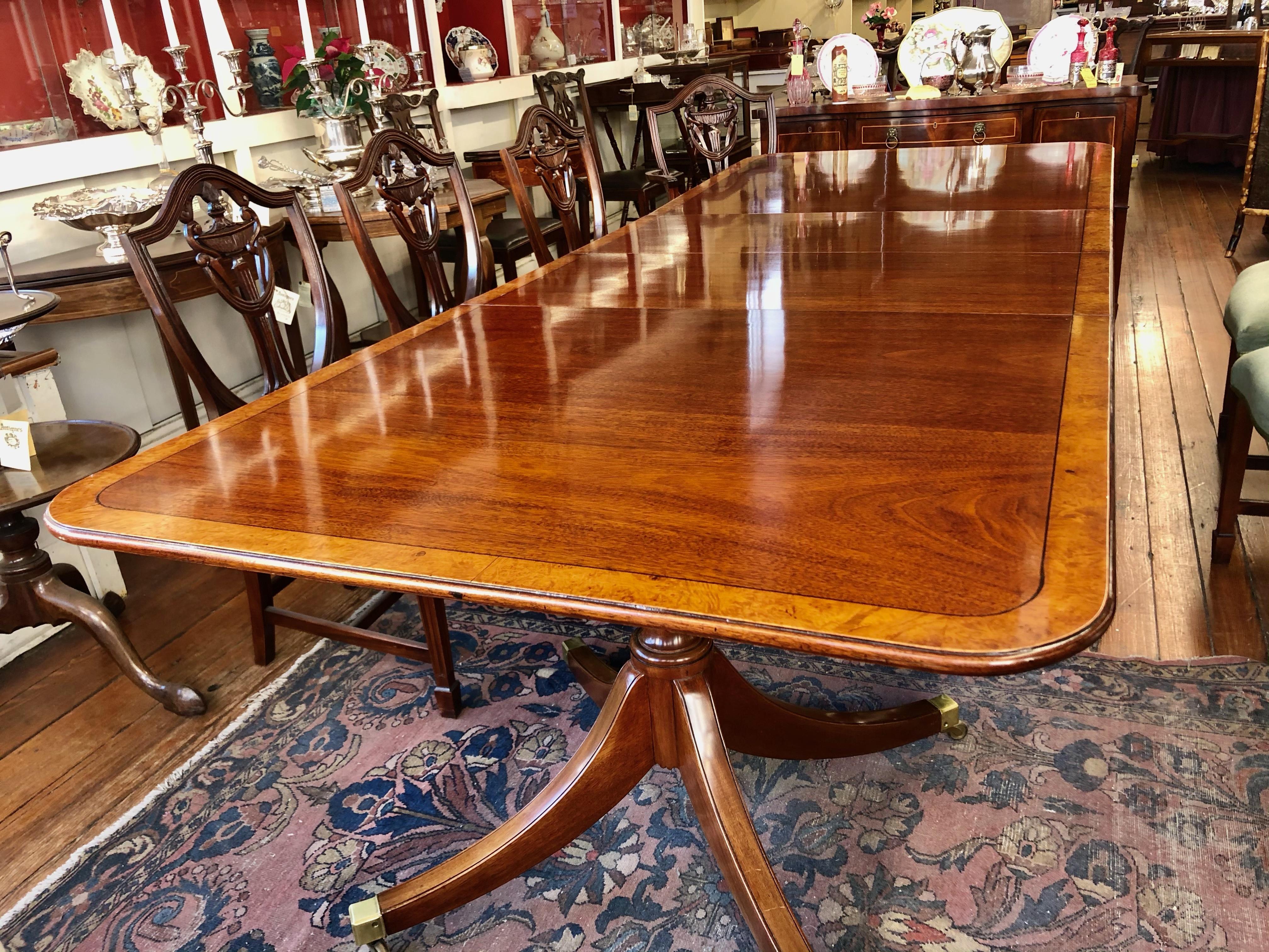 Superb Old English Inlaid figured mahogany Regency or Sheraton style two pedestal two leaf dining table with extraordinary burr walnut crossbanding (inlay) and quad splay leg pedestal with solid brass cap toes and brass casters. Circa 1930-'40.

 