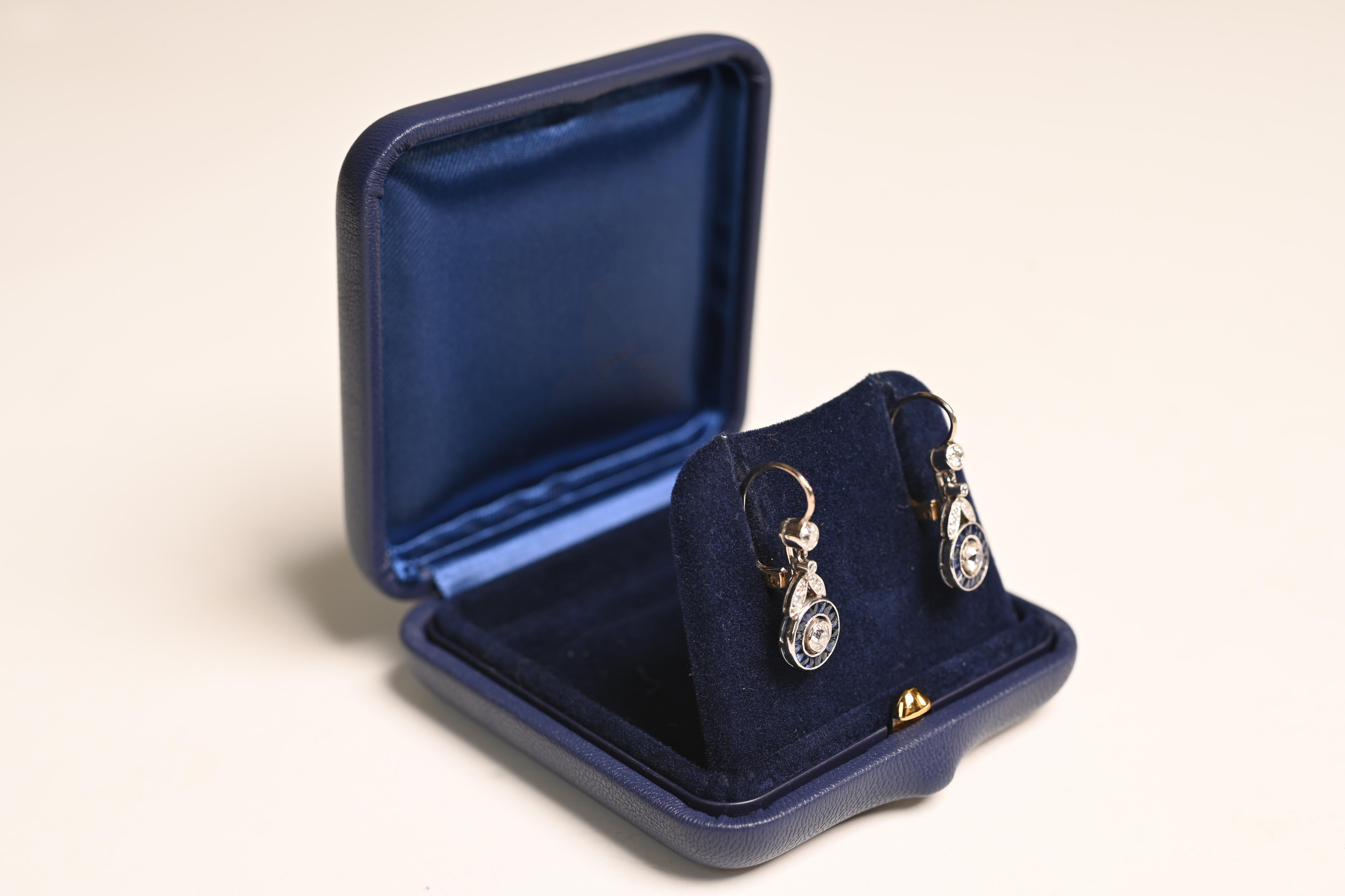 Superbe paire de boucles d'oreilles pendantes en platine, chacune centrée sur un diamant de taille européenne ancienne pesant environ 0,10 carat. Les diamants du bas sont entourés d'un halo de saphirs naturels taillés à la française, offrant un