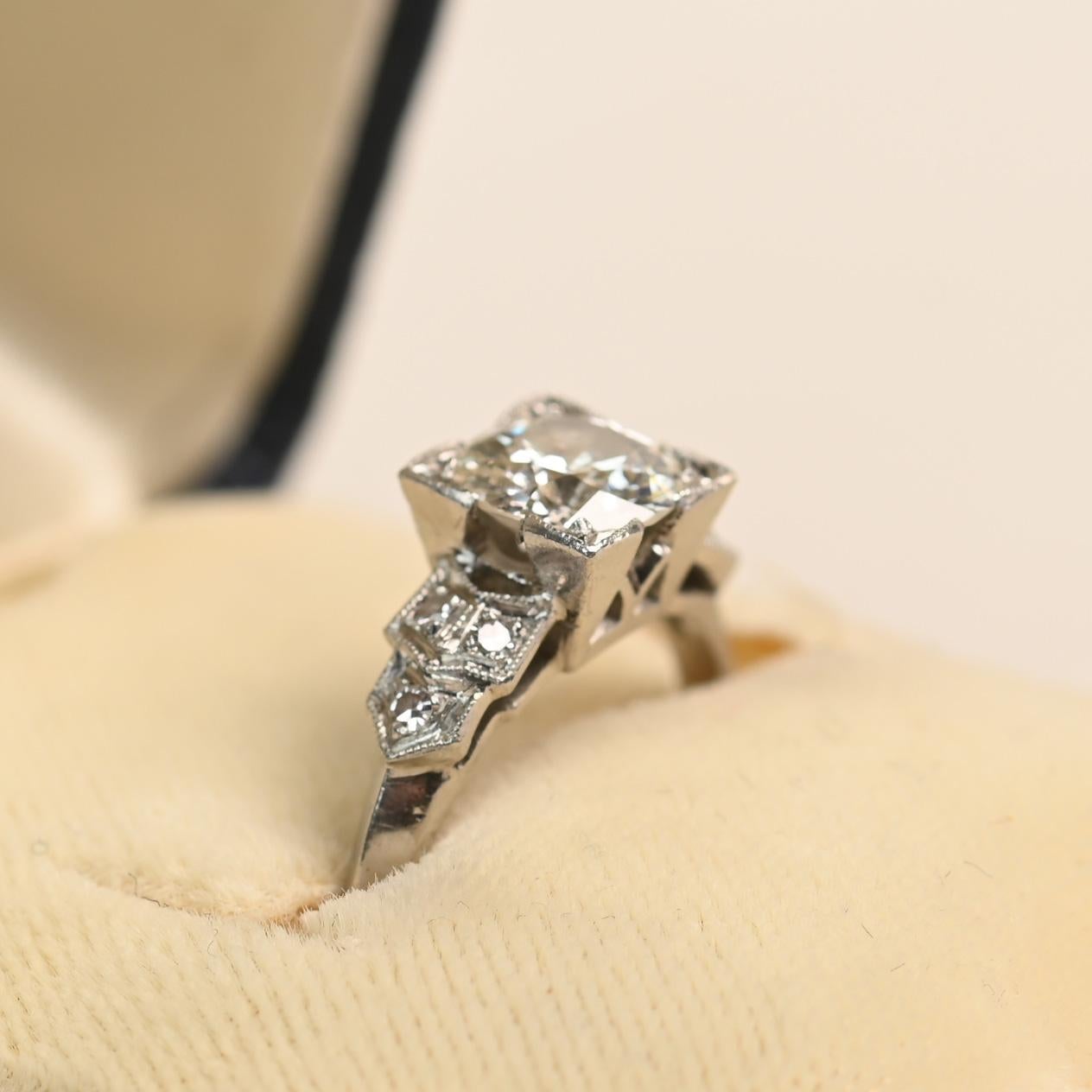 This exquisite Art Deco ring centers an old European cut diamond weighing approximately 0.9 carats, graded J color and VS1 clarity. The diamond is secured in a square prong setting, enhancing its brilliance while giving the design a bold,
