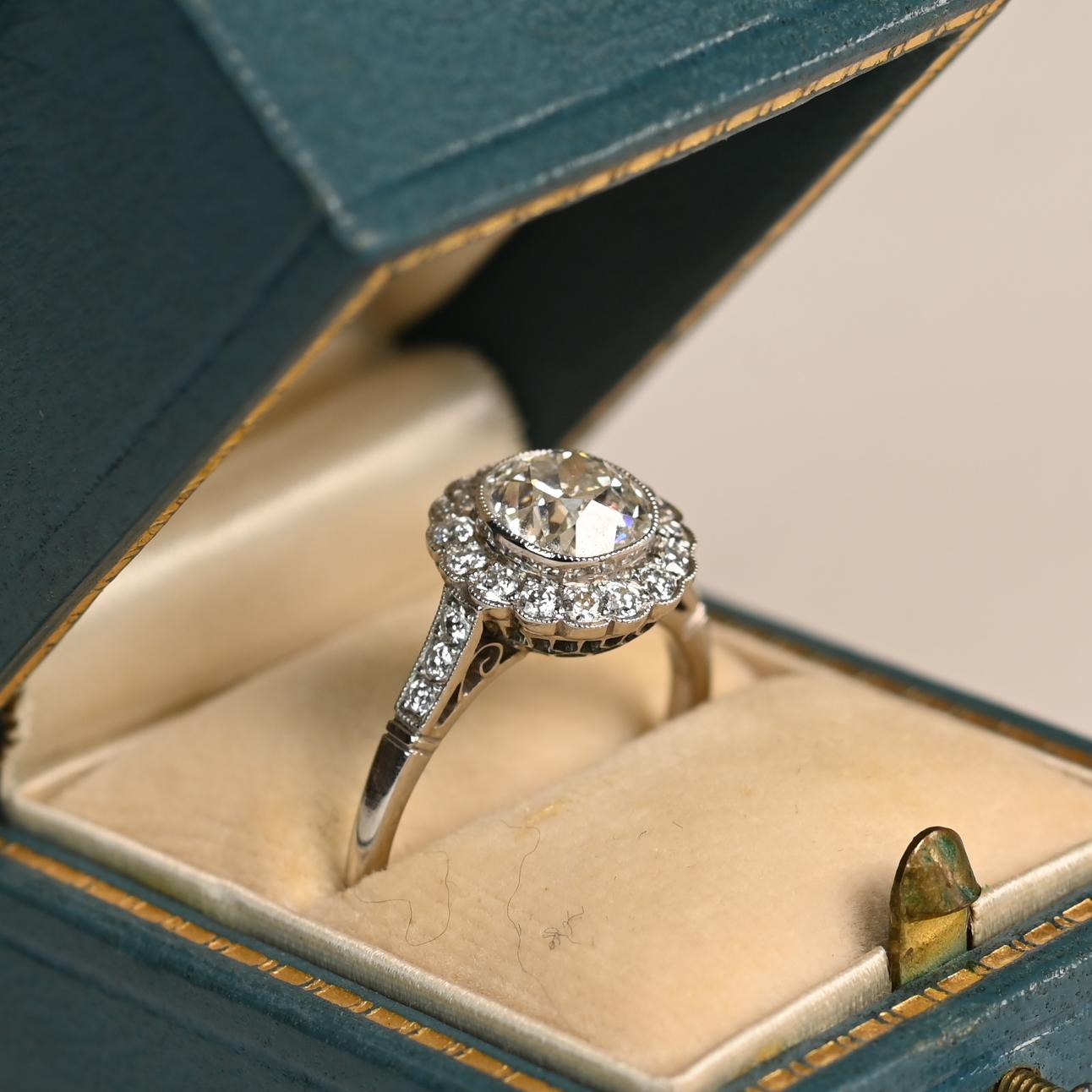Este exquisito anillo en racimo de diamantes exhibe en su centro un impresionante diamante de talla europea antigua de aprox. 1,30 quilates, de color J y claridad excepcional VS1. Alrededor de la pieza central hay un halo de diamantes adicionales de