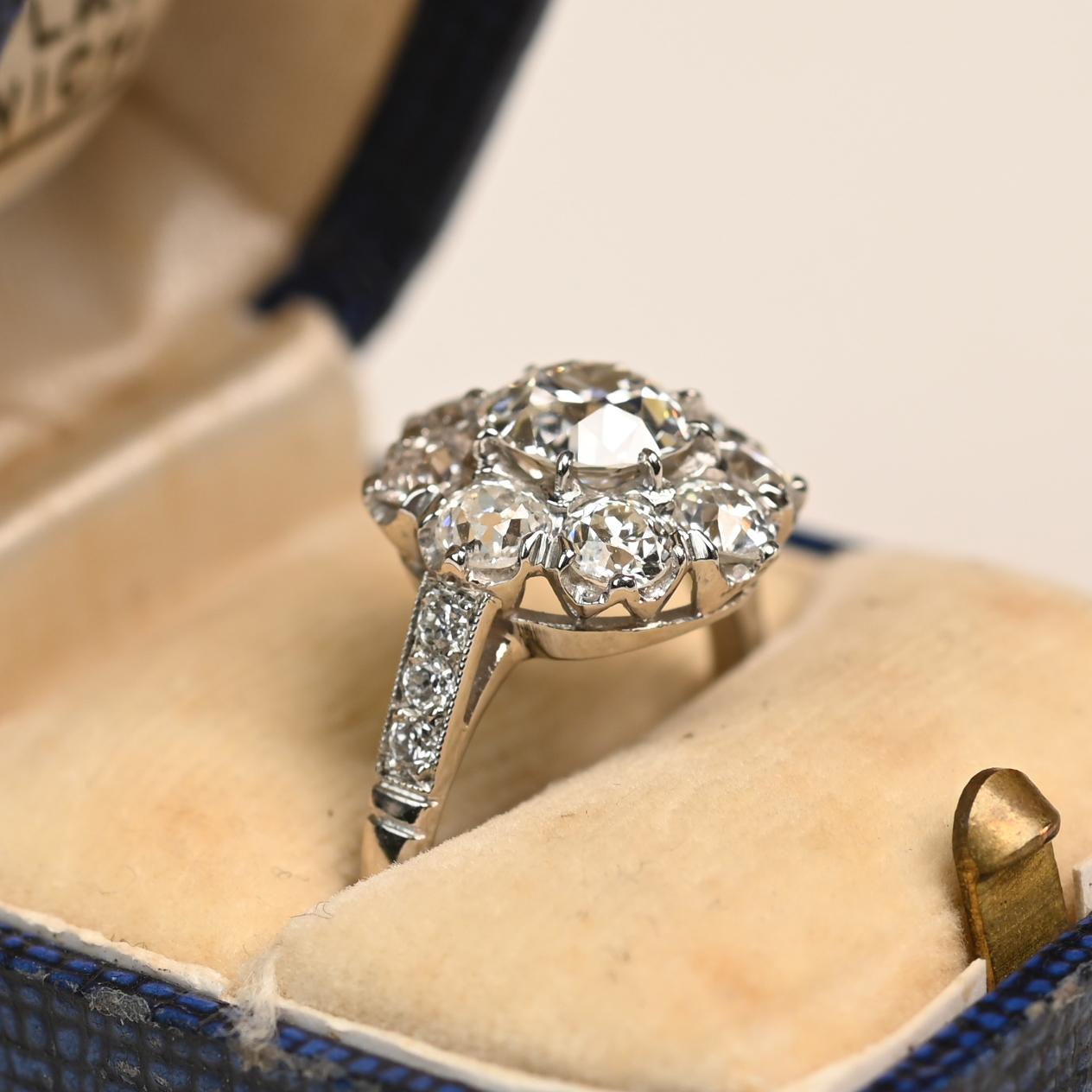 Cette exquise bague à grappes de diamants est centrée sur un diamant de taille européenne ancienne certifié par la GIA, pesant environ 1,00 carat, de couleur G et de pureté VS2. La pierre centrale est encadrée par une grappe florale de diamants de