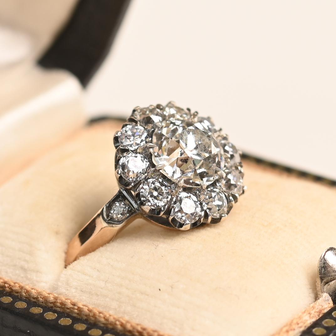 This floral diamond cluster ring showcases a GIA-certified Old European cut center diamond weighing approximately 1.5 carats, graded J color and SI2 clarity. Set in prongs, the primary diamond is surrounded by a halo of Old European cut diamonds