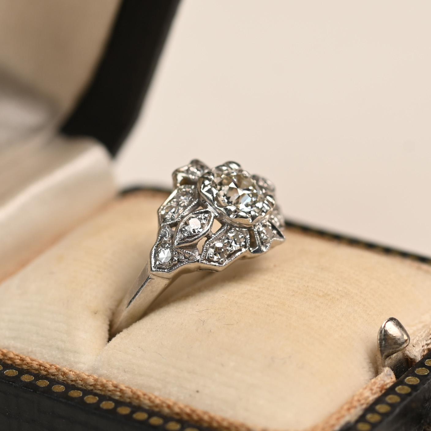 An exquisite Art Deco ring showcasing an approximately 0.50-carat Old European cut diamond, graded J color and VS1 clarity. The center diamond is framed by a geometric filigree design, adorned with additional Old European cut diamonds. These accent