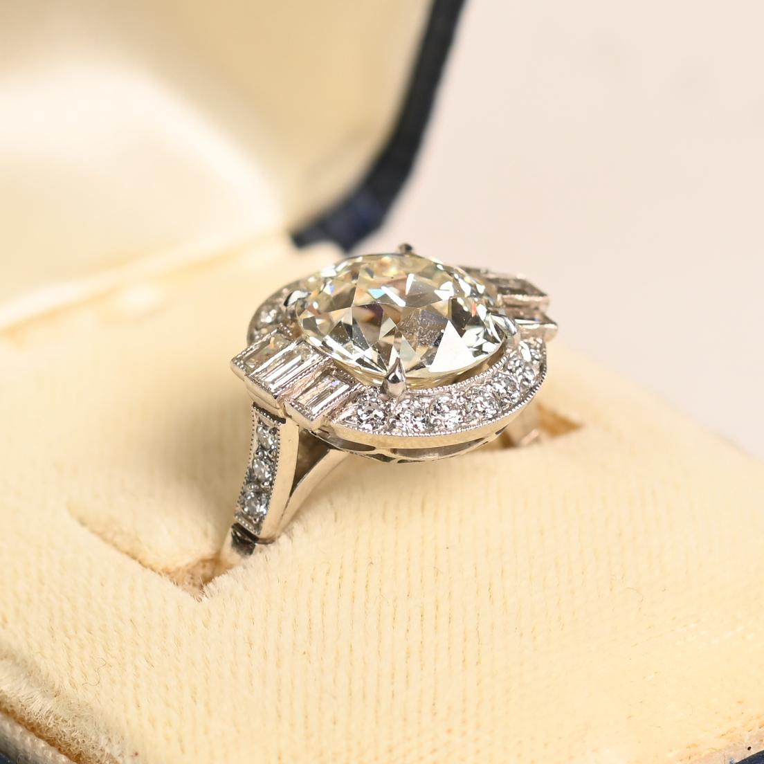 Questo squisito anello di fidanzamento presenta al centro un vibrante diamante vecchio taglio europeo da circa 3,8 carati, colore K, purezza VS2. L'affascinante pietra centrale è splendidamente incorniciata da un delicato alone di diamanti più