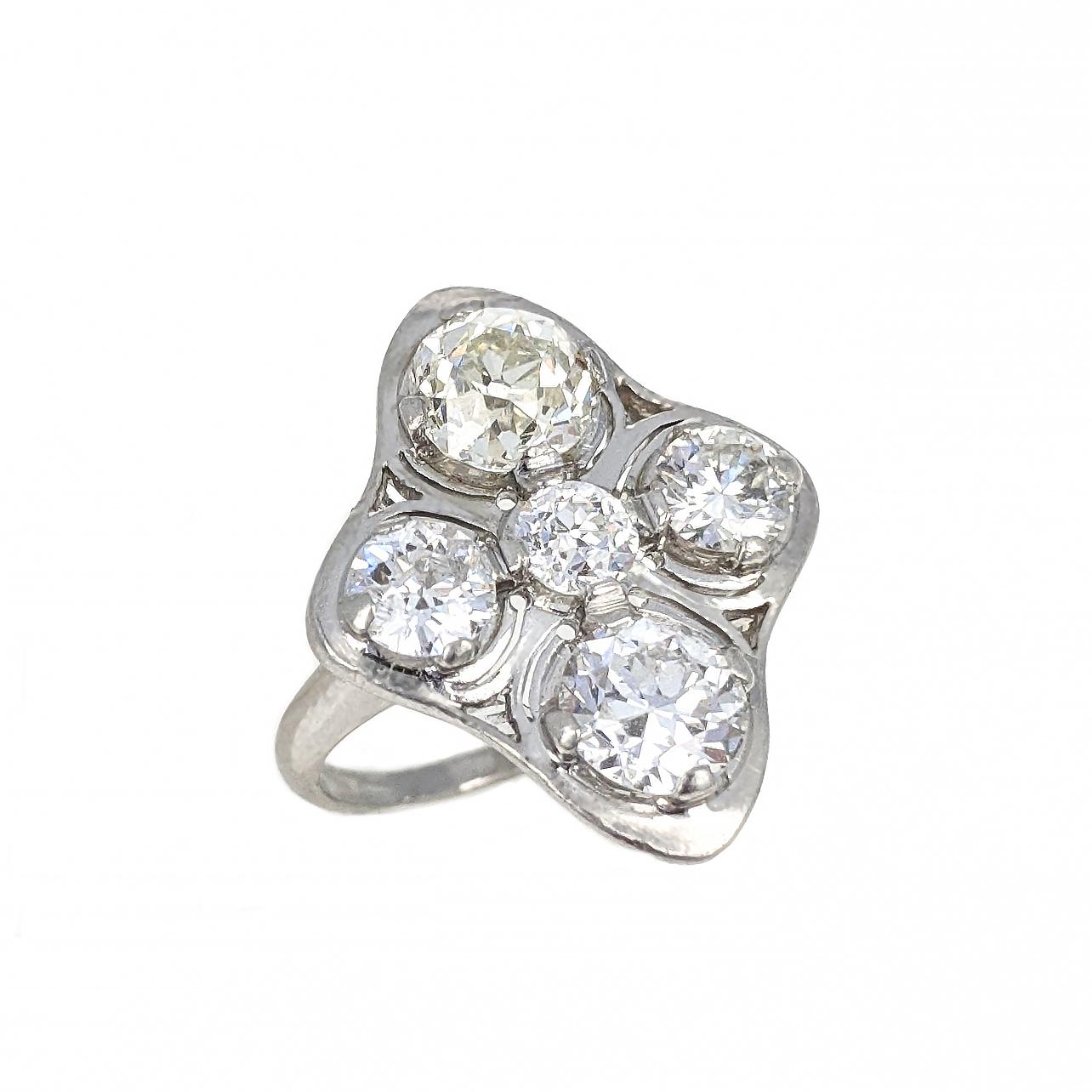 This ring features four Old European cut diamonds weighing approximately 2.2 carats and one round brilliant cut diamond weighing approximately .3 carats. It is mounted in platinum with openwork details. The top of the ring measures 2.5 x 2 cm. Size