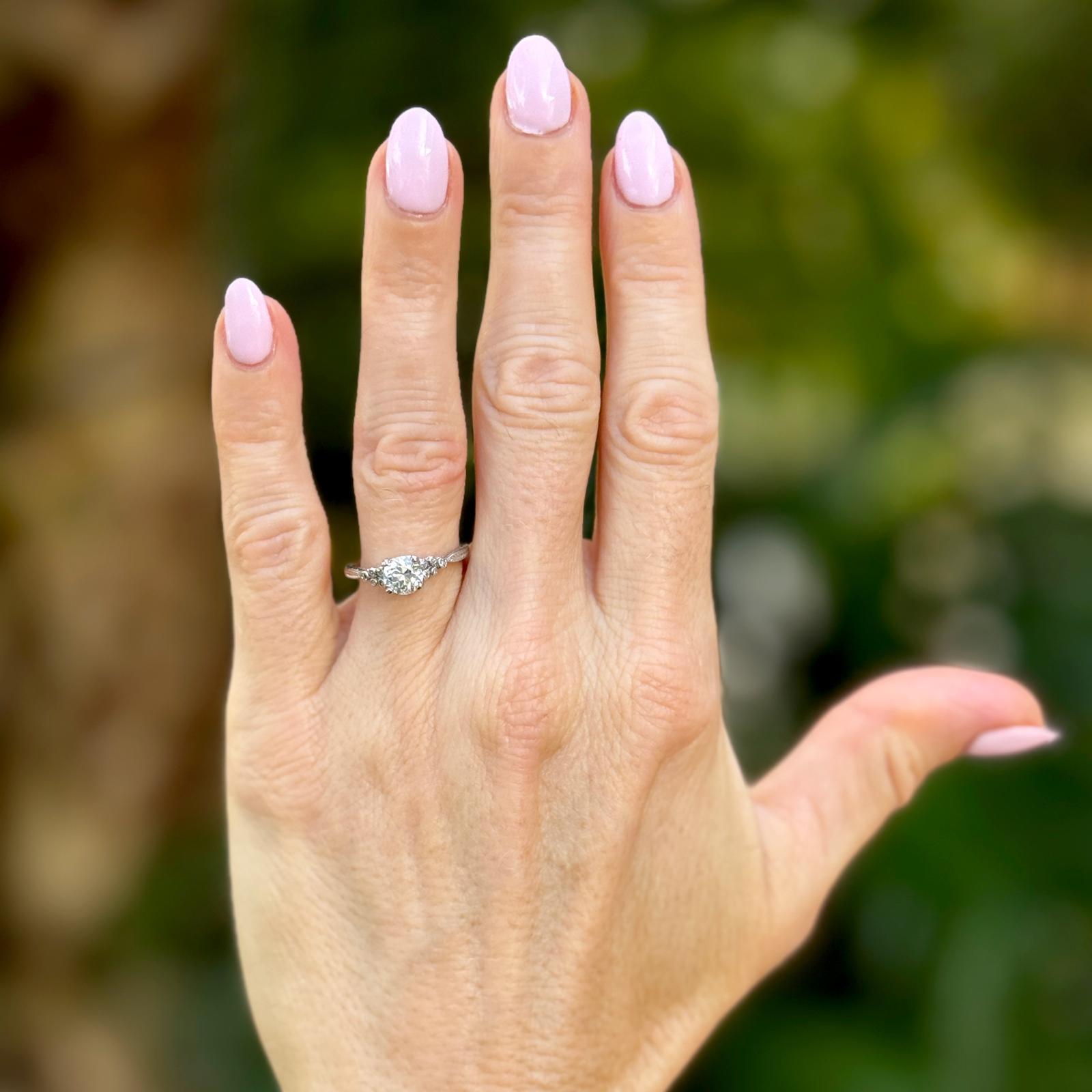 Dieser Vintage-Verlobungsring aus Platin zeigt in der Mitte einen fesselnden Diamanten im alten europäischen Schliff von ca. 0,82 Karat, mit der Farbe J und der Reinheit SI1. Der Mittelstein ist in Zacken gefasst, so dass seine antiken Facetten das