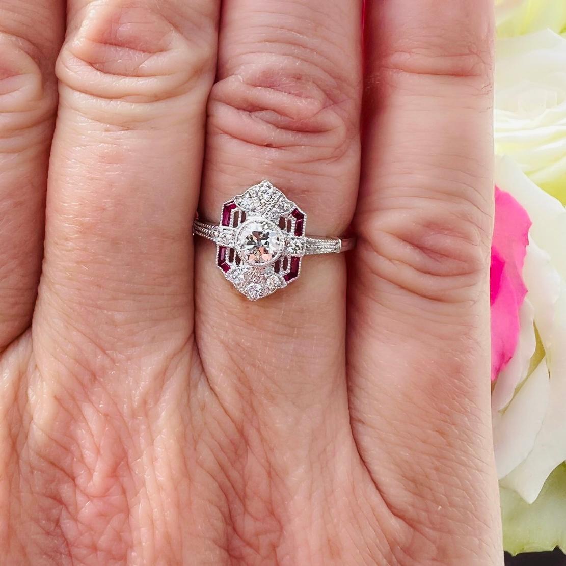Design reminiscent of an era where design really mattered! This Art Deco inspired white gold stunner features a 0.42 carat Old European Cut Diamond at the center, bezel set amidst fine white melee diamonds and expertly cut rubies, forming a gorgeous