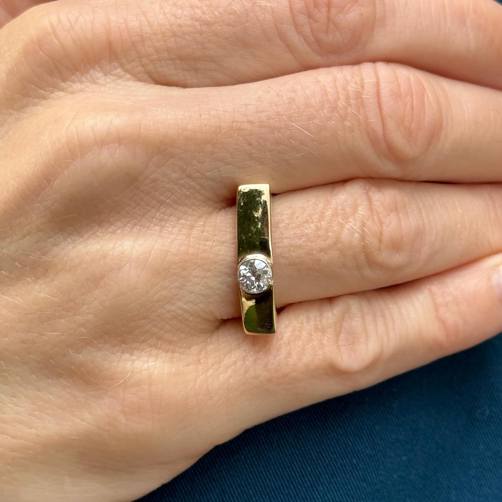 Bezel set diamond band ring crafted in 18 karat yellow gold. The ring features a single Old European cut diamond weighing approximately .50 carat and graded G color and SI1 clarity. The squared off band measures 5.5mm in width and is currently size