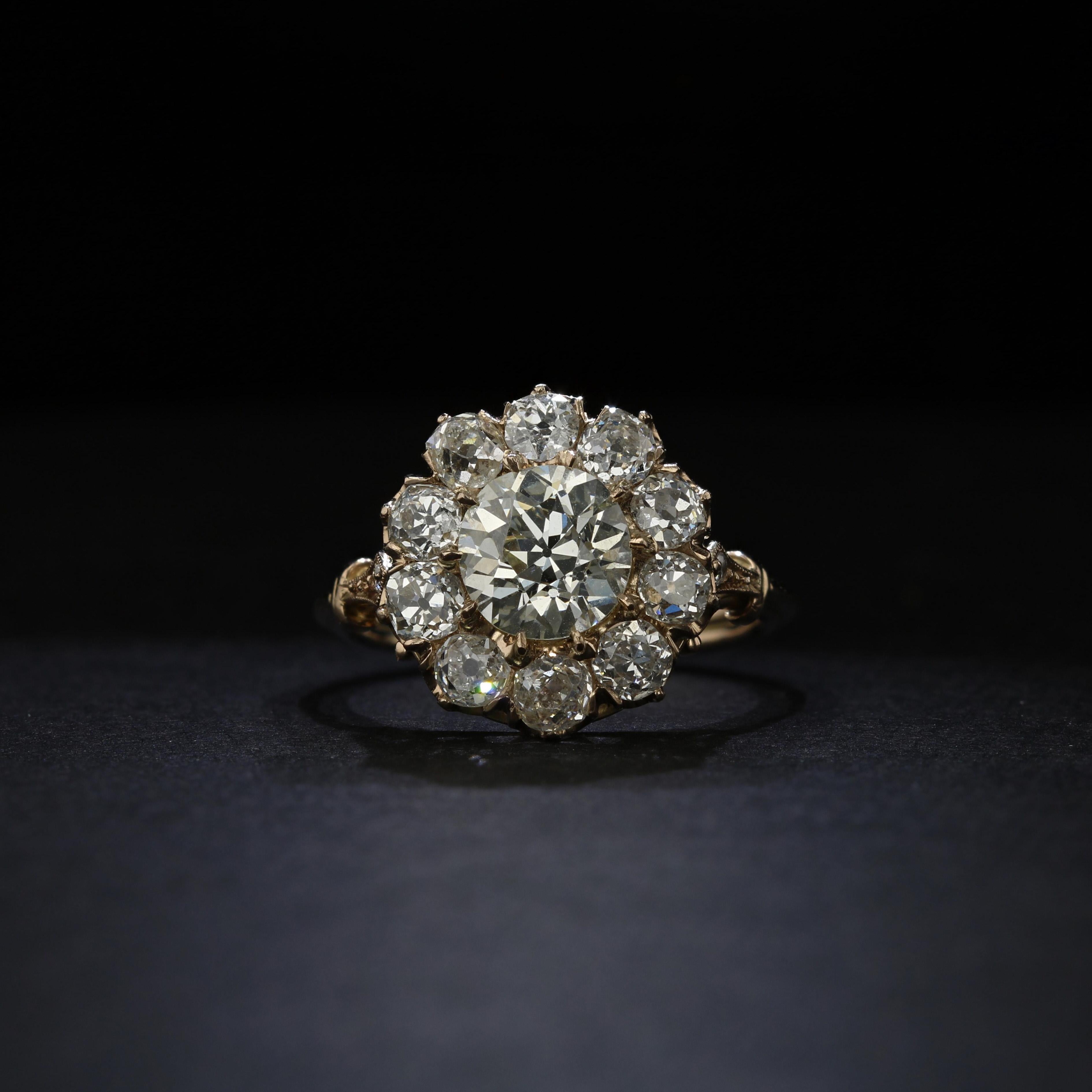 Ten old mine diamonds surround a stunning 1.70 carat Old European diamond in this estate cluster ring handmade in 14k yellow gold. An extra diamond, along with elegant scrollwork and millegrain detailing is set in each shoulder of the ring. A