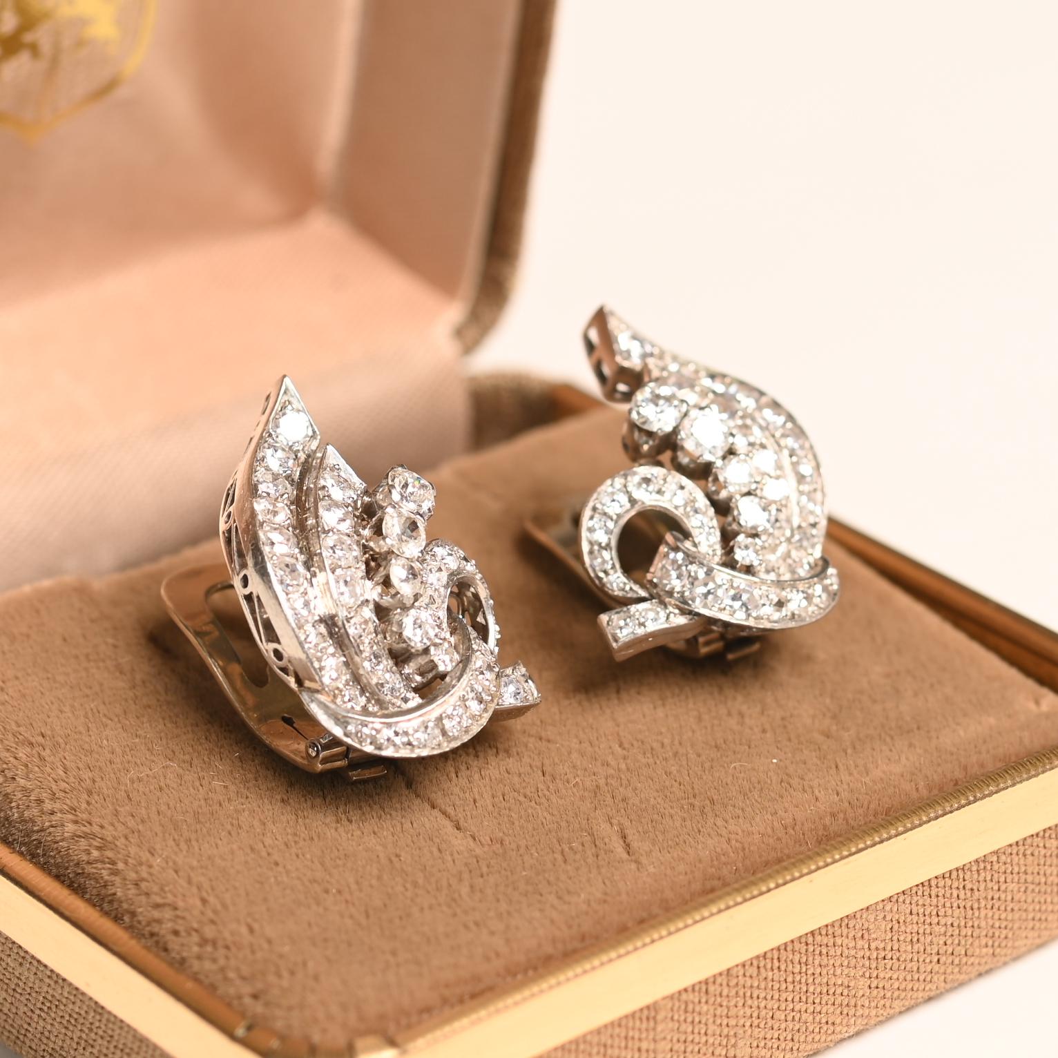 Un par de pendientes vintage de diamantes realmente exquisitos, meticulosamente elaborados a mano en platino durante la época de mediados de siglo, hacia 1950. Estos elegantes pendientes muestran un sofisticado motivo de volutas, con cintas