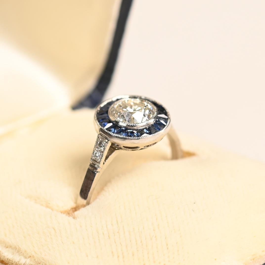 Cette exquise bague halo en diamant et saphir est ornée d'un captivant diamant de taille européenne ancienne d'environ 0,70 carat, de couleur J et de pureté SI2. Le diamant central est solidement serti, ce qui permet à son charme vintage d'occuper