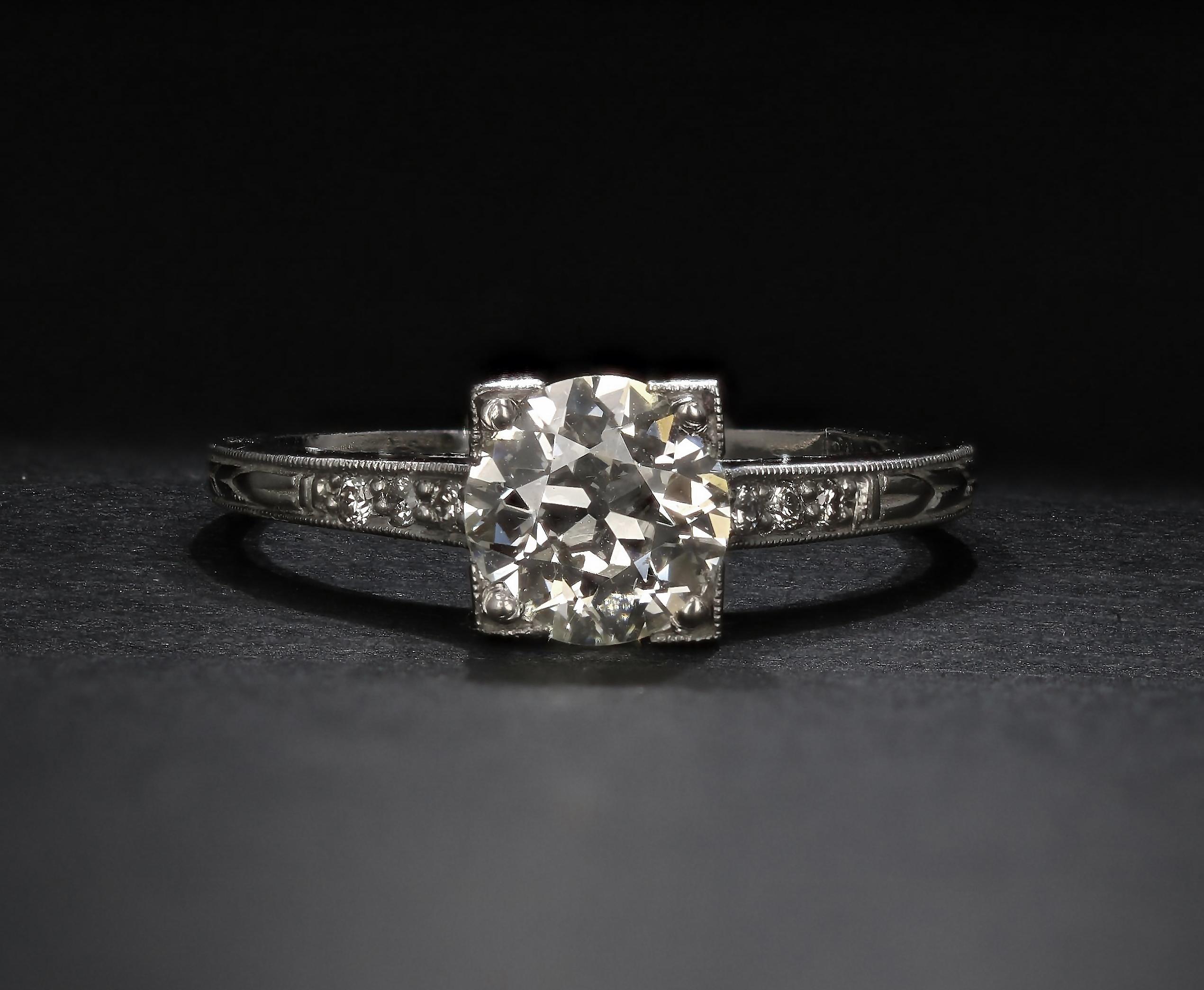 In the center of this estate diamond engagement ring is an Old European diamond of more than one carat. The ring is crafted in platinum and features fine engraving on the shank. A half dozen smaller round diamonds accent the ring's sides. 

DIAMOND
