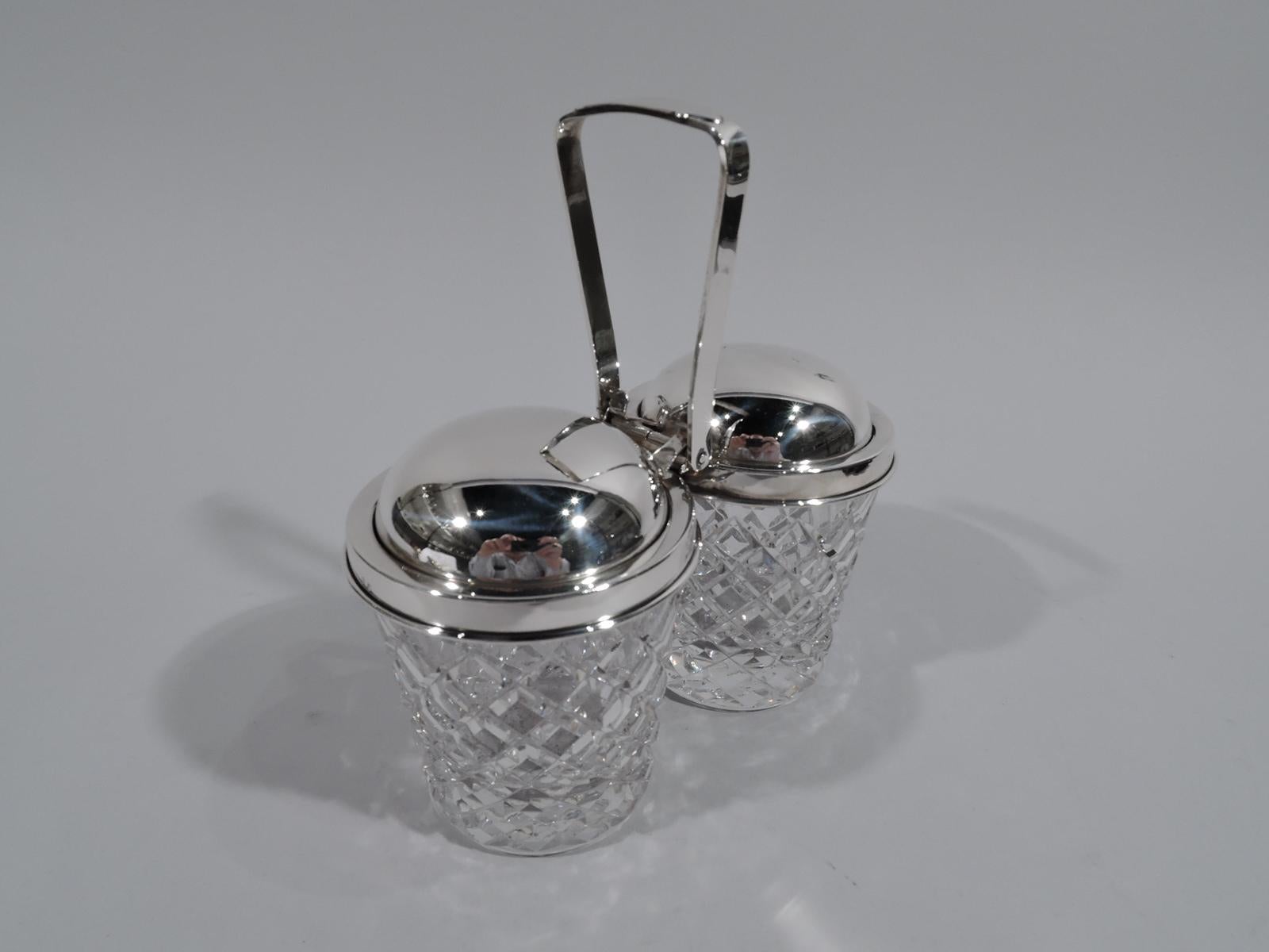 Old-fashioned sterling silver and glass double jam jars. Retailed by Cartier in New York, circa 1950. Two jars each with straight and tapering sides and raised diaper pattern. Sterling silver collars joined by mount with tapering swing handle. Domed