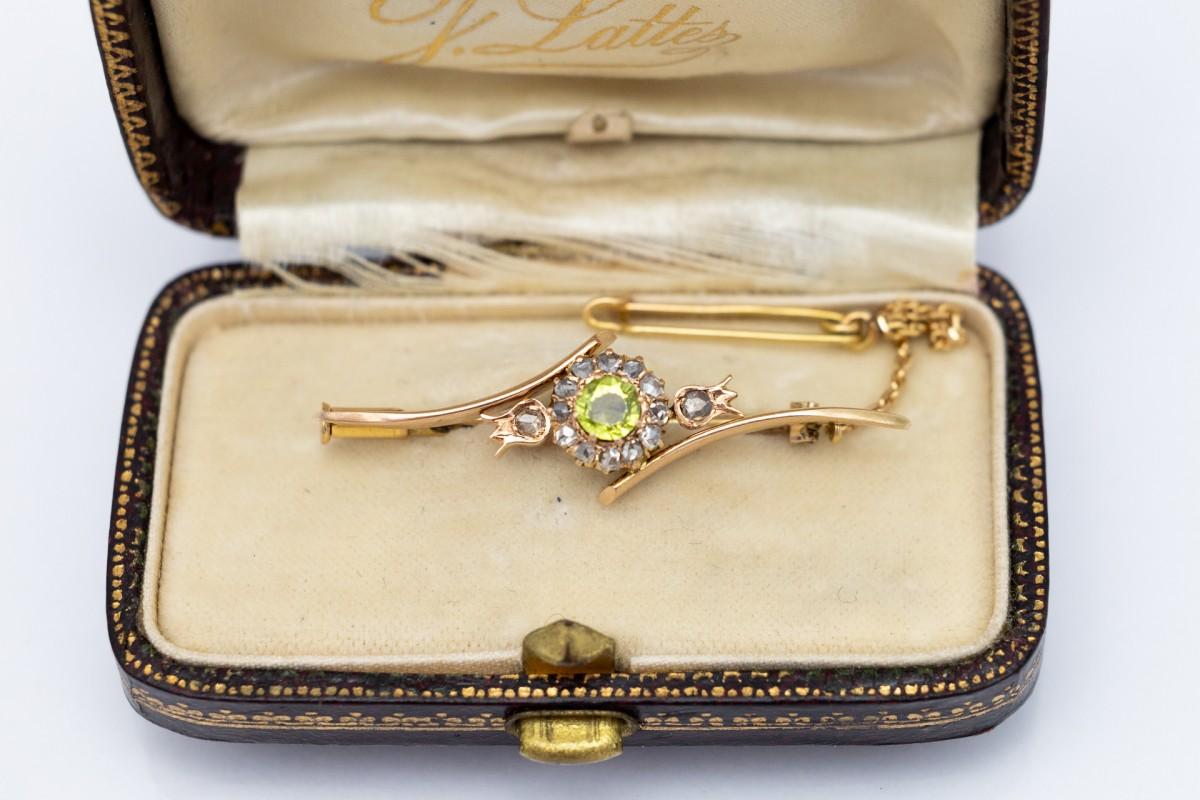 Elegante spilla in oro giallo 14 carati (finezza 0,585). Olivina centrale, chiamata anche peridoto, del peso di circa 0,50 carati, circondata da 14 diamanti taglio rosa con un peso totale di 0,30 carati.

Spilla con spilla da balia