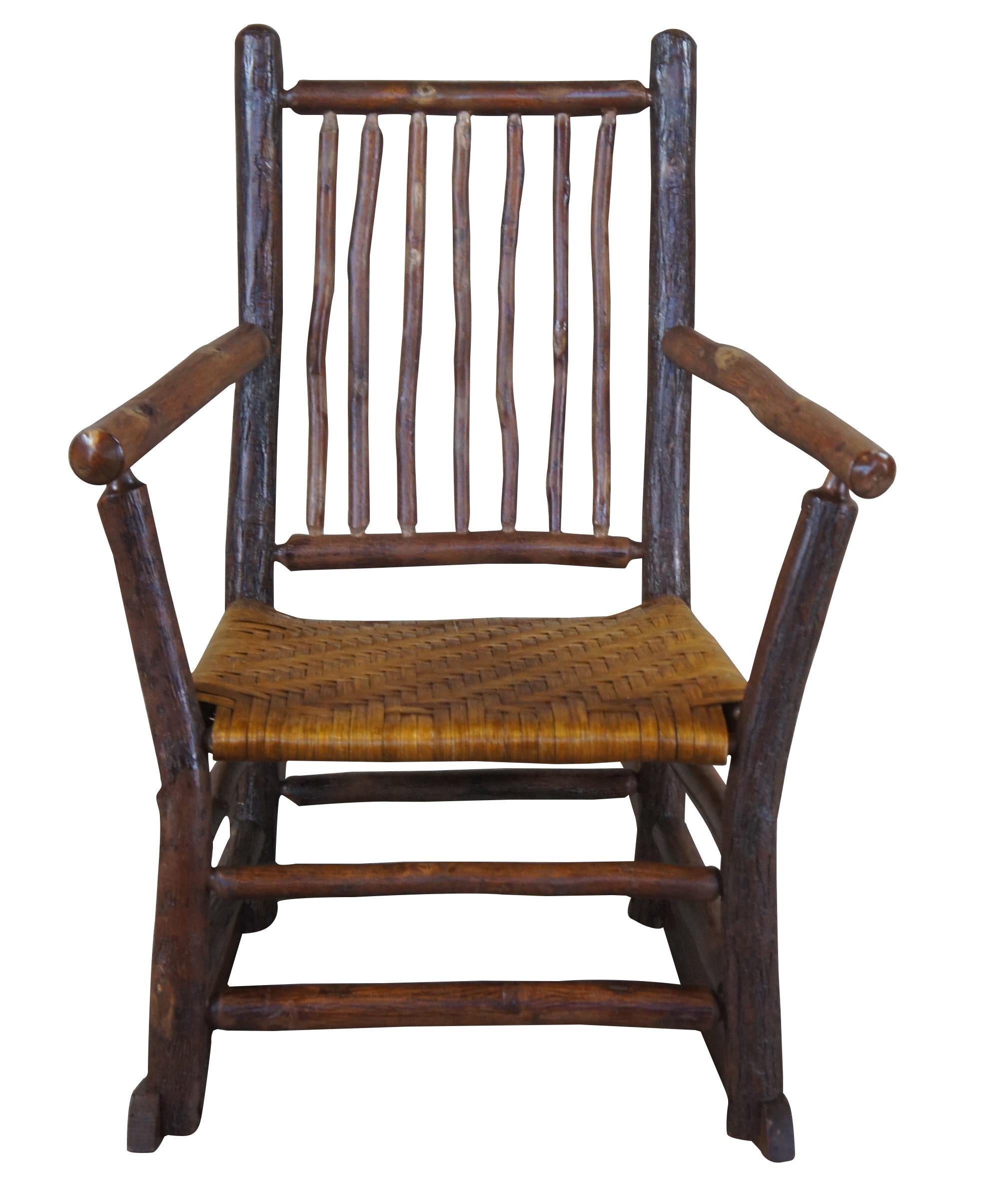 Antique circa 1930s #25 rocking chair by Old Hickory Furniture Company of Martinsville, Indiana. Features a primitive Adirondack style with flared arms and rattan seat. 

History
In the 1800's as pioneers traveled West across America, they