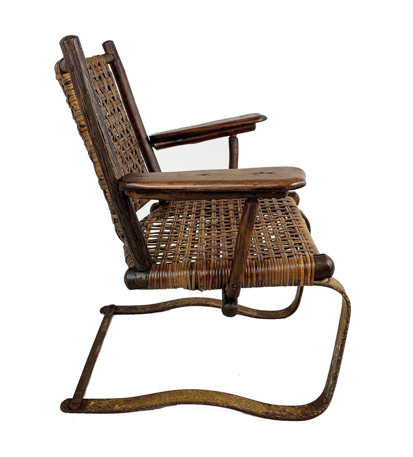 Old Hickory spring chair with a metal base and woven seat and back. The seat was rewoven at some point with narrower cane. It has a wide seat, rounded back, wide arm rests, and bounces on its metal frame, so it is sort of like sitting in a rocking