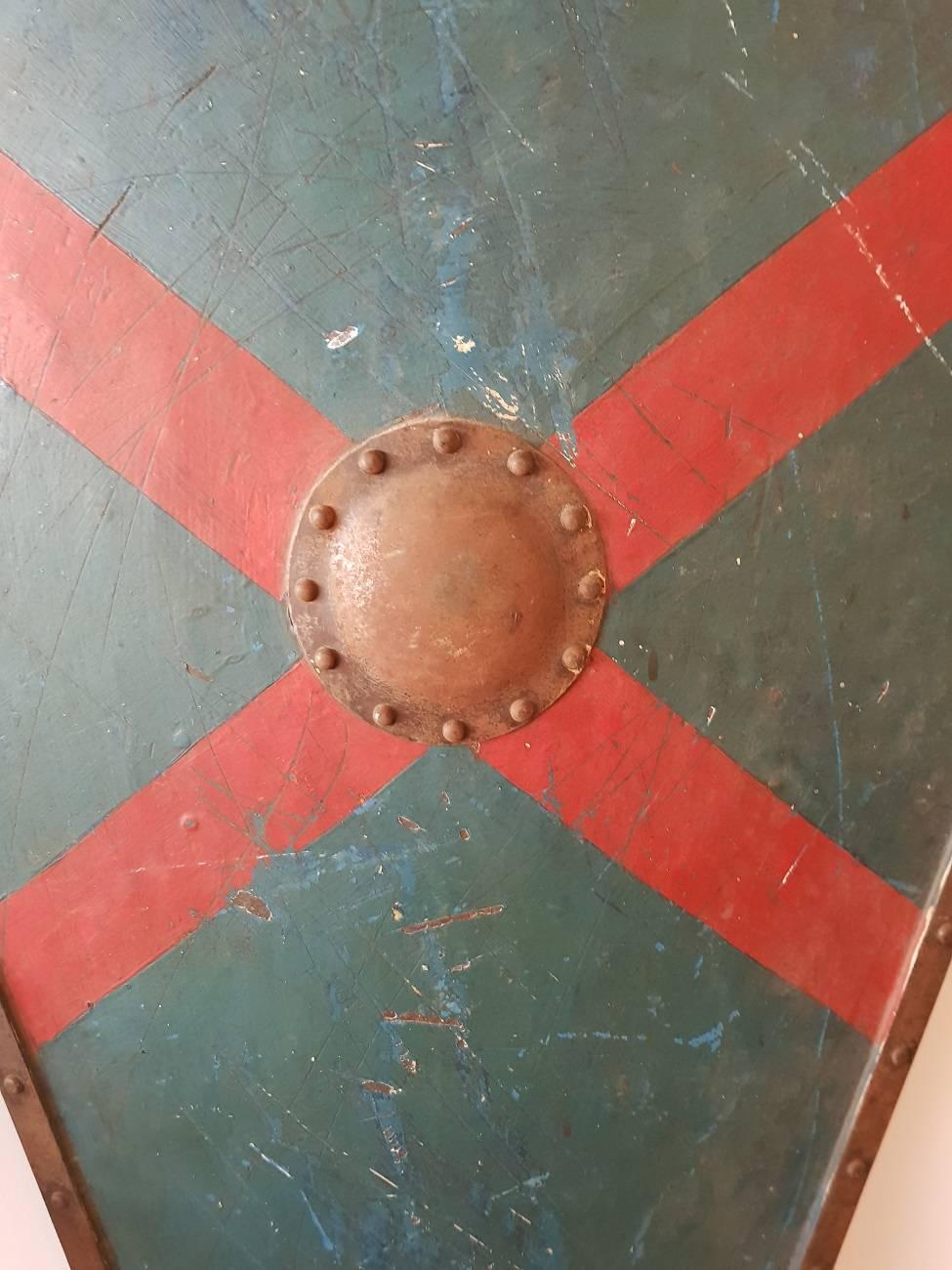 Medieval style metal kite shield model from circa 1900 to a sample that were made in the 10th to the 13th century, decorated with a red X on blue background.

It weighs around the 7 kilo's and the measurements are:
Depth 5.5 cm/ 2.1 inch.
Width