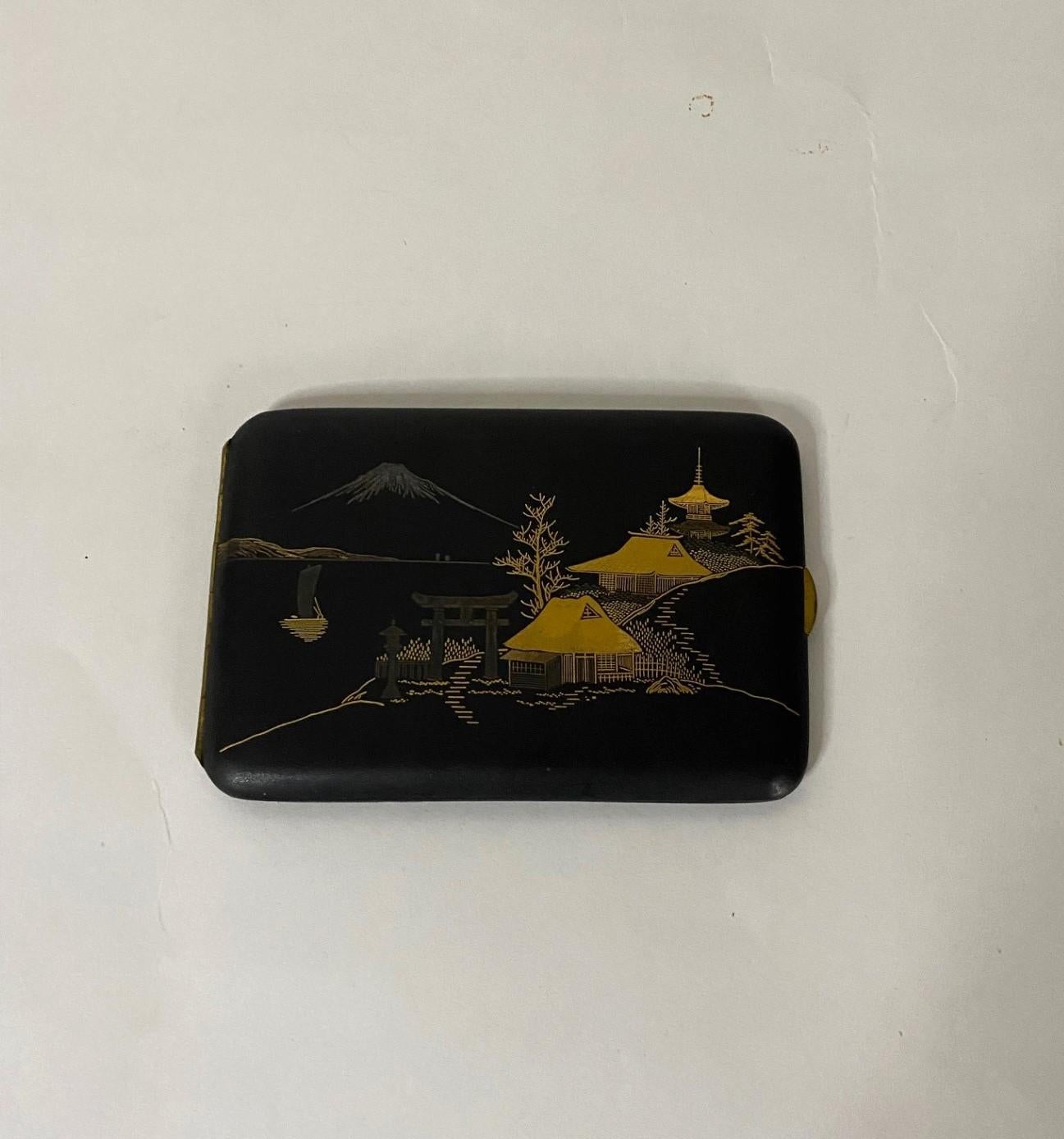 Make an impressive elegant statement with this early 20th century unique Japanese brass cigarette case.  The sleek black folding case has a artistically etched scene on its cover.