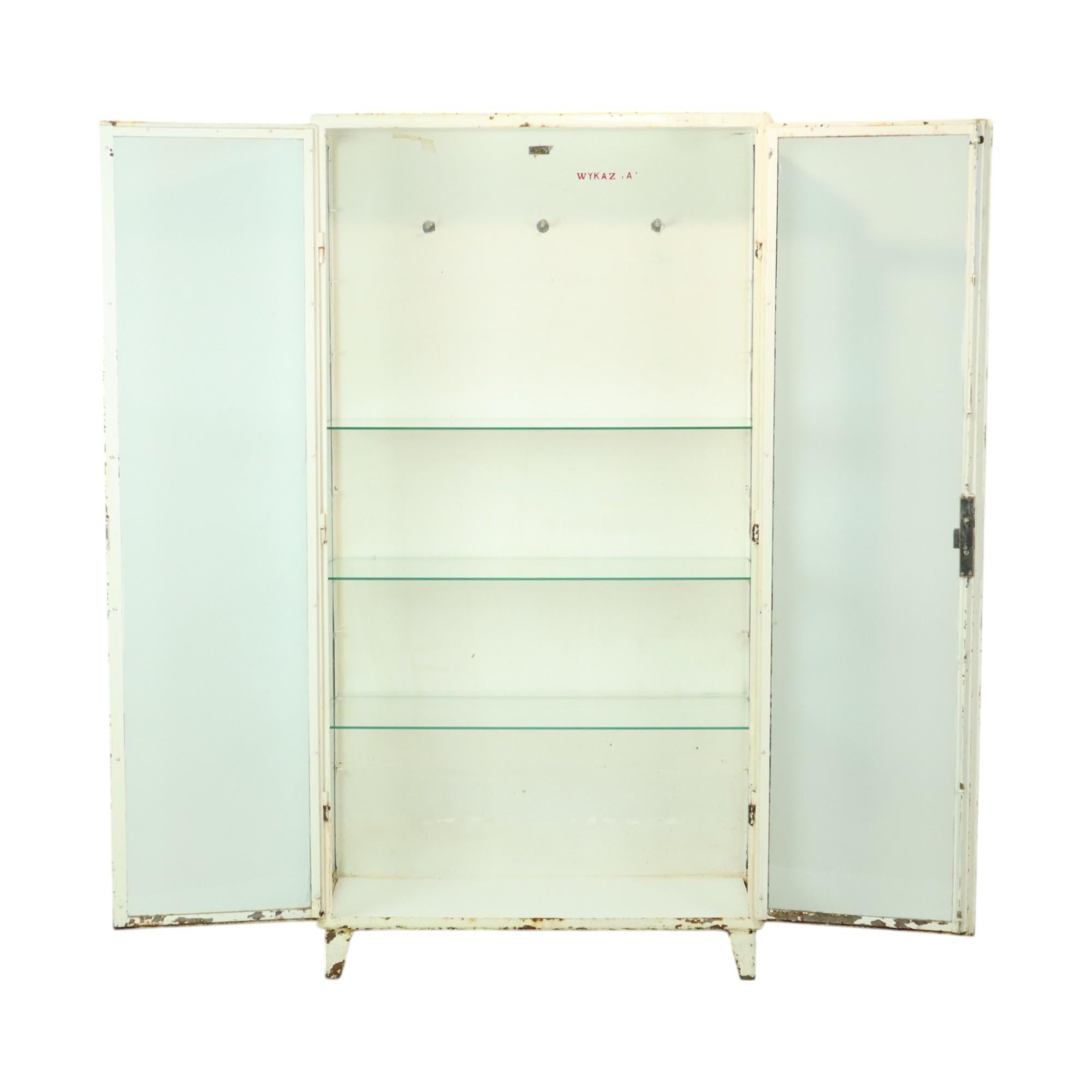Antiguo gabinete de farmacia, botiquín, fabricado con armazón de metal pintado de blanco y cristal, tiene 3 estantes nuevos rectificados de cristal templado de 6 mm, marcado Spoina Lublin, fabricado en Polonia en los años 60.

Precioso mueble