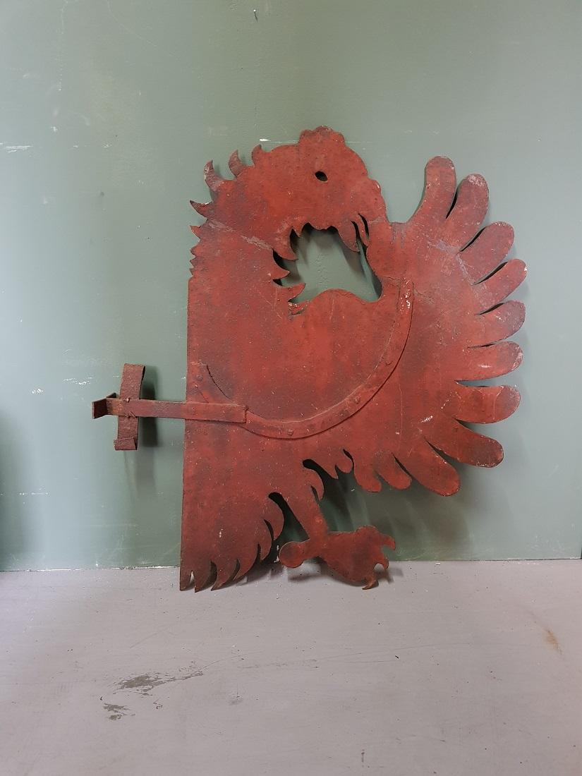 Old metal signboard with an image of a half eagle with a bracket attached to it in old red color, otherwise in a good condition only weathered by age. Early 20th century perhaps even late 19th century.

The measurements are,
Depth 65 cm/ 25.5