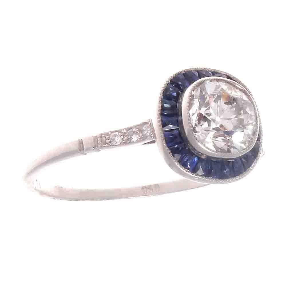 A stylish recreation from the art deco era. Featuring a lively 0.92 carat old mine cut diamond surrounded by a halo of vibrant blue sapphires. A colorful and well made ring, lovingly hand crafted in platinum.
Ring size 7 and may easily be re-sized