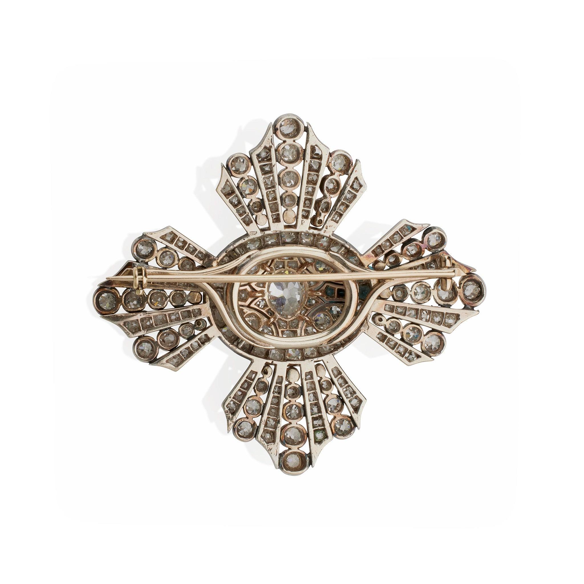 This stylized antique cross brooch set with approximately 14.30 carats of old diamonds dates from circa 1870. It is designed with a domed oval center with flaring, lobed arms, mounted in dark patinated silver and low karat gold. A dramatic design of