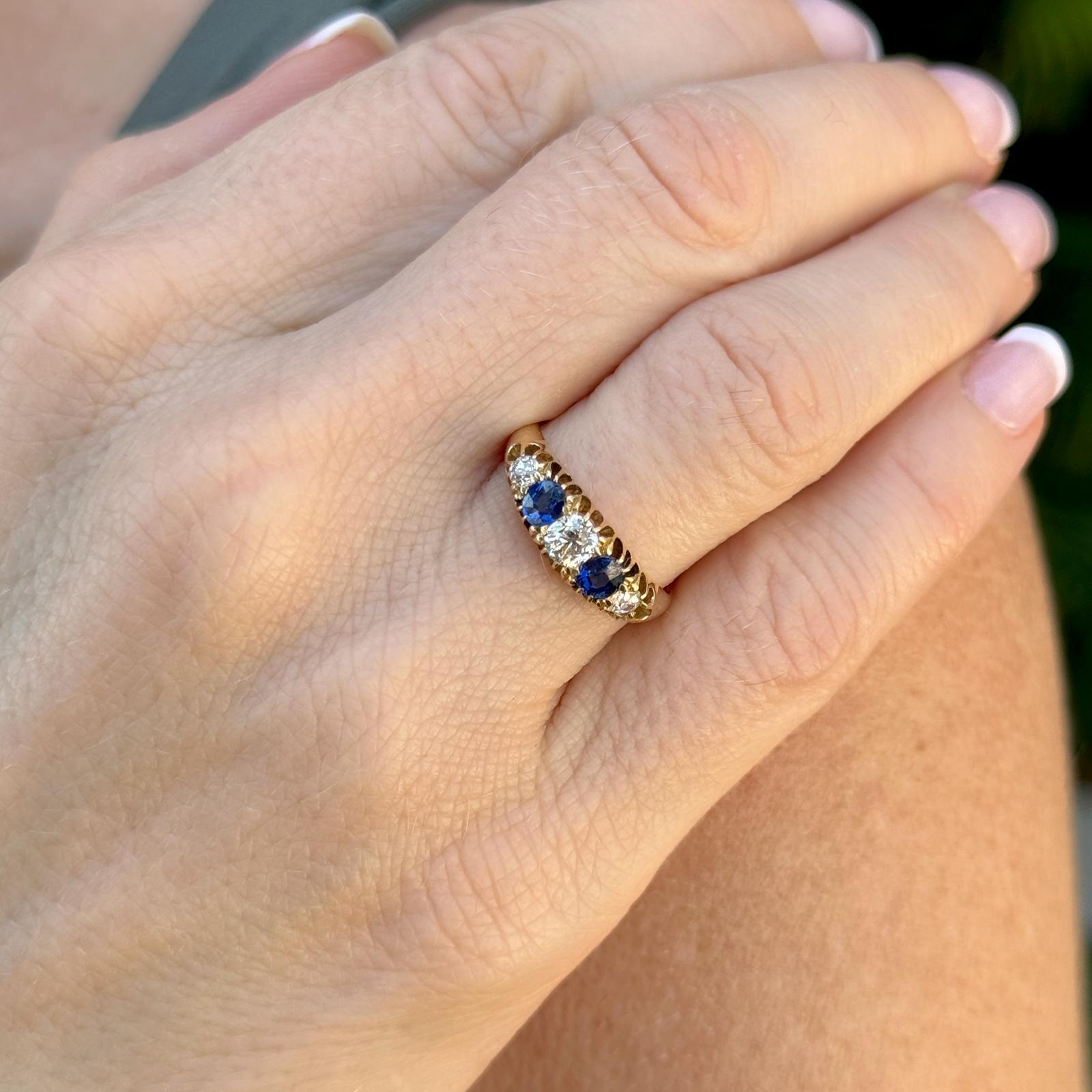 This vintage 5-stone band ring exudes classic beauty and timeless elegance. Crafted from rich 18 karat yellow gold, the ring features a stunning arrangement of 3 old mine cut diamonds and 2 vibrant sapphires. The diamonds weigh approximately .40