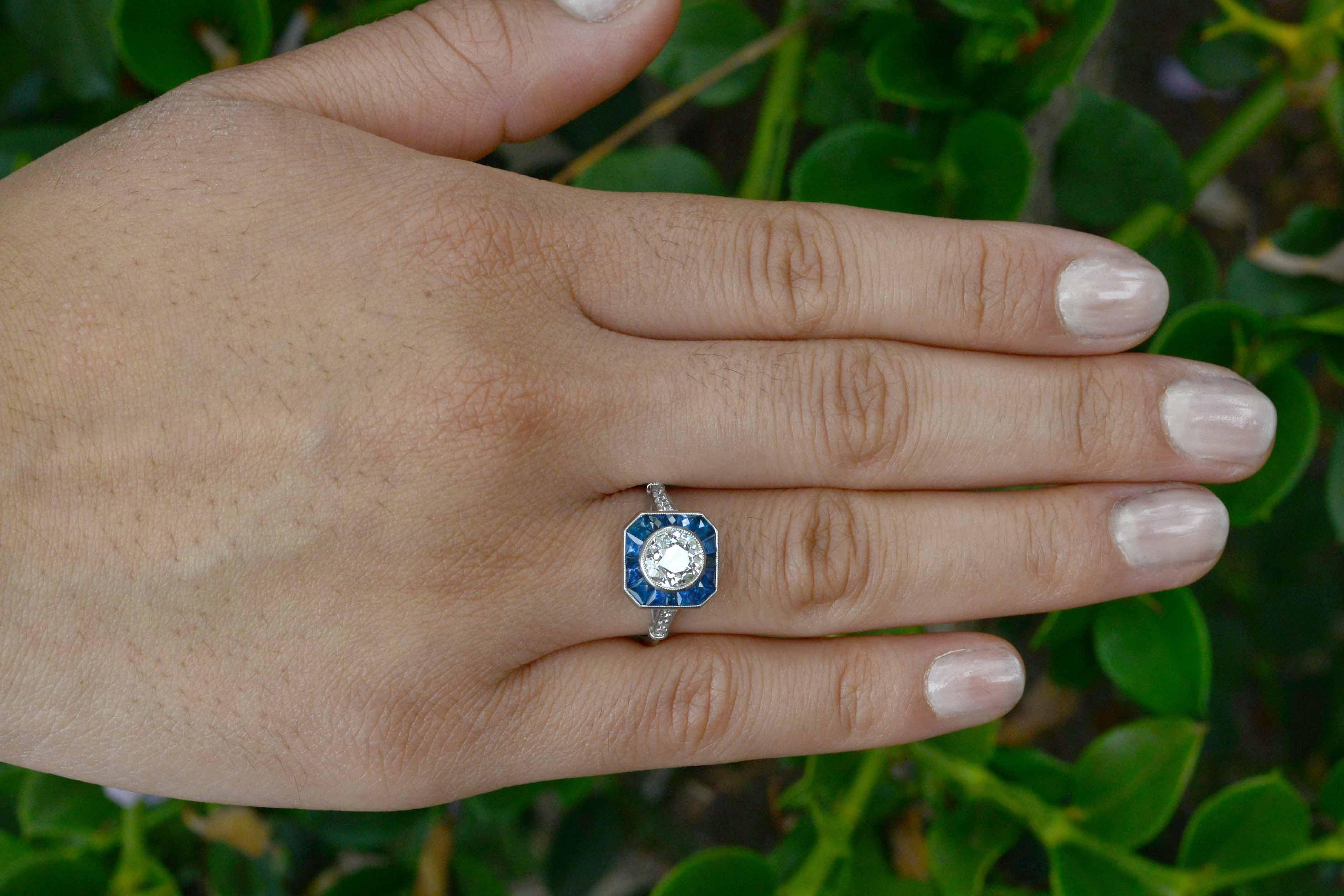 A blazingly beautiful 1.25 Carat antique, old mine cut diamond of a crisp, icy near-colorless white is surrounded by a platinum and blue sapphire halo in a sleek octagon shape. Entirely hand made (with a 