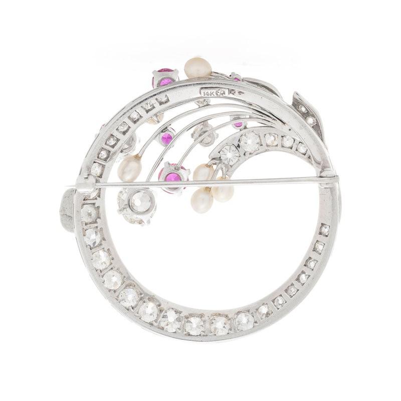 This wreath style brooch delicately features two old mine cut diamonds, weighing approximately 1 carat, alongside numerous old mine cut diamonds, five round mixed cut rubies, and six cultured pearls, all mounted in 14 karat white gold. 

Stamp: 14K