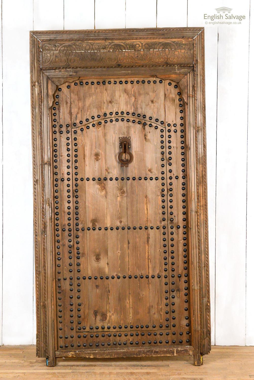 Old Moroccan door with a wicket gate / Judas door in a carved frame. Metal studs and old door knocker. One side of the door is plain. Some splits and scuffs with separation to part of the frame. Frame measures: 124cm x 228cm x 10cm. Outer door