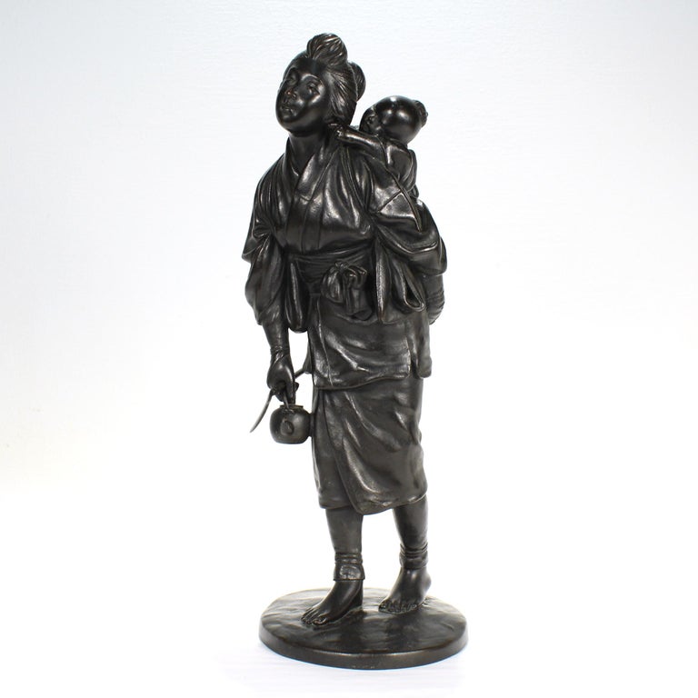 A fine antique Japanese bronze statue.

Depicting a woman holding a teapot and sickle in one hand while carrying her baby on her back with the other hand. The laughing baby is tugging on the ear of his gently smiling mother. 

The piece has a