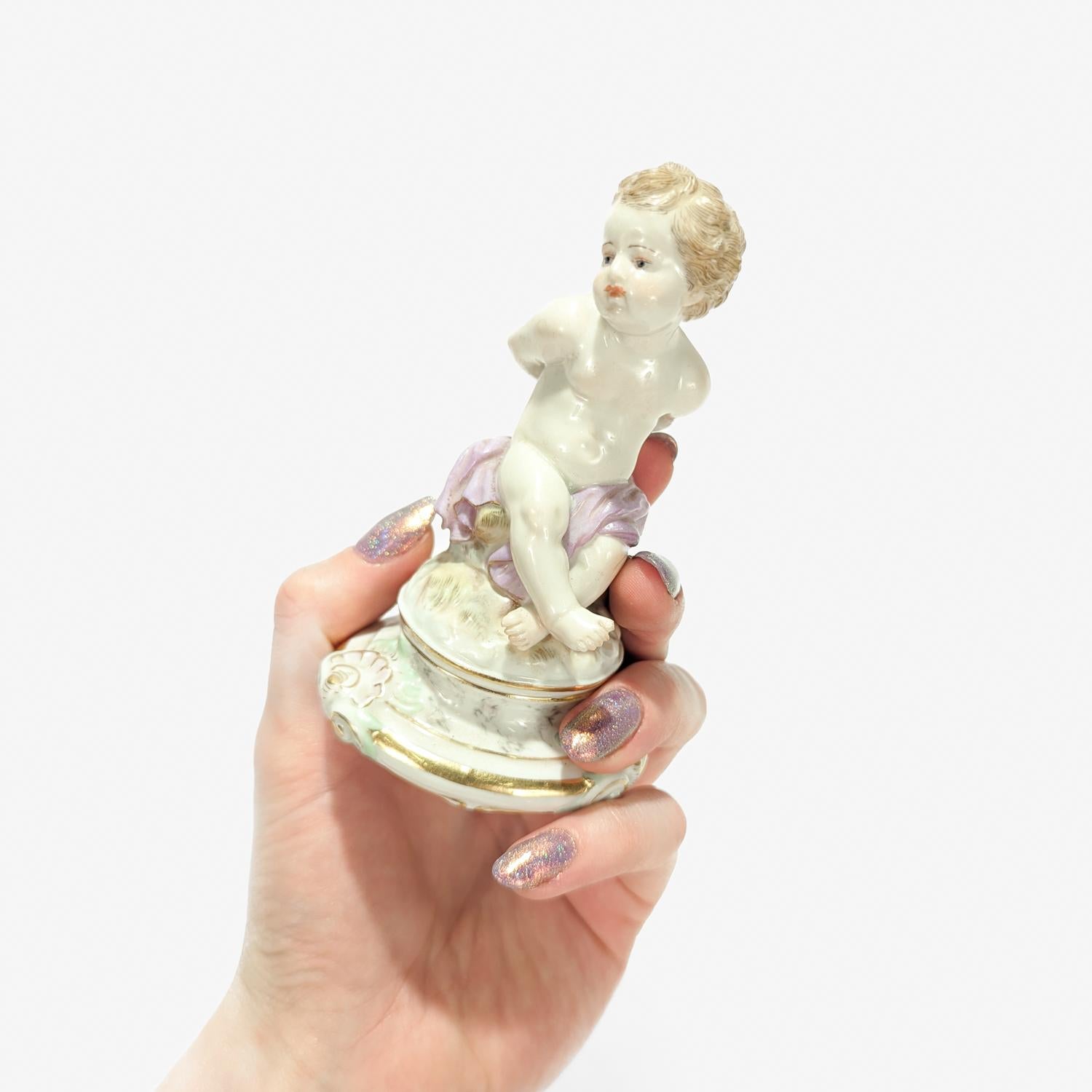 Fina figurita de porcelana de Meissen antigua o vieja.

Representa a Cupido sentado sobre una roca con expresión triste, con las manos y las alas atadas a la espalda.

Sobre un zócalo circular rococó dorado. 

Model No. L102.

Según el modelo