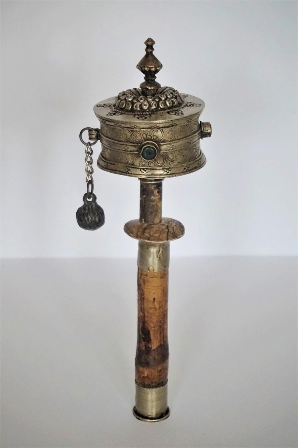 An old exclusively handmade Tibetan hand held prayer wheel, Tibet, early 19th century. The handle is of wood with silvered metal fittings. The cylinder is of embossed silvered metal with red and green stones. Inside of the cylinder there is a