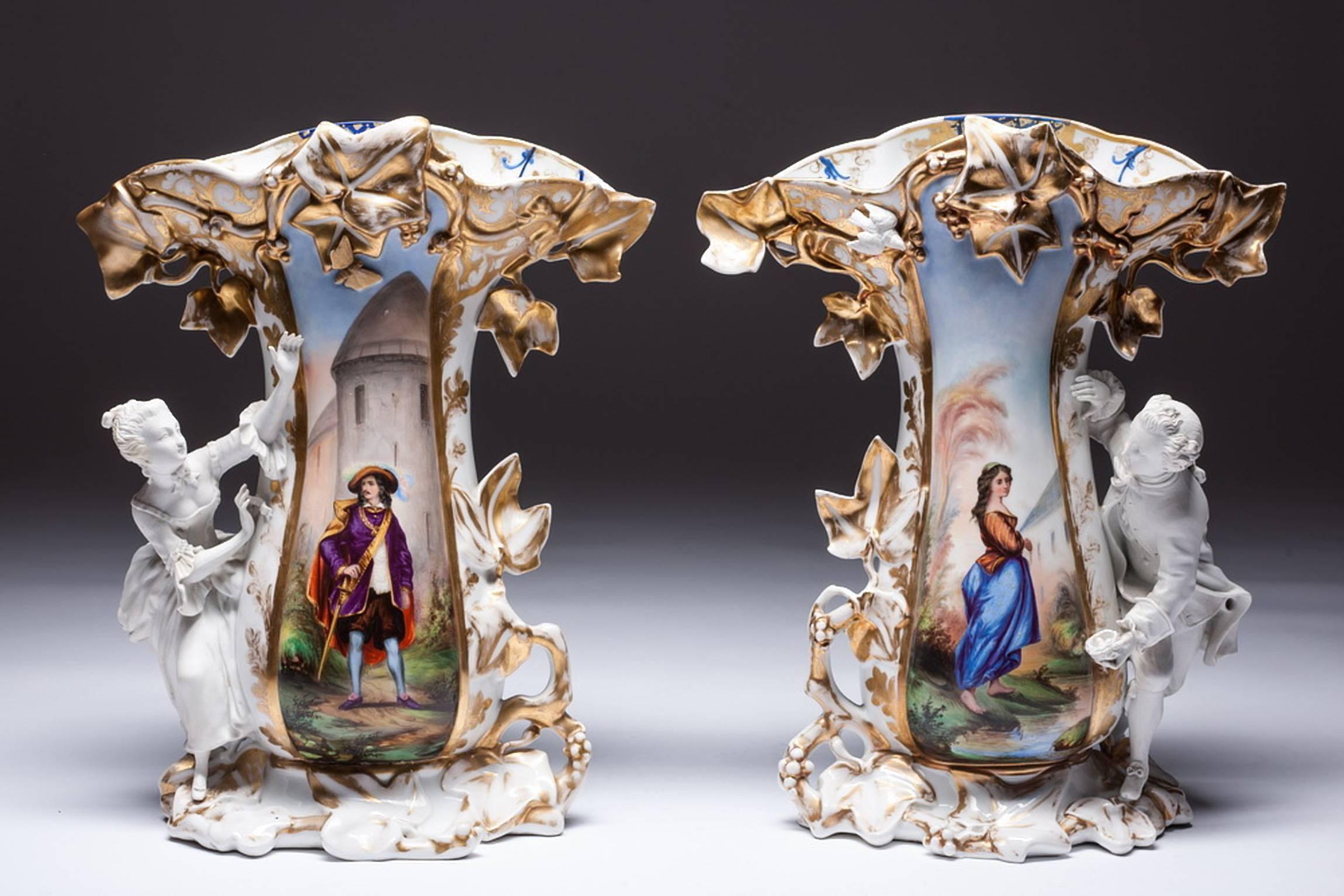 Both vases is with bisque figurines on the sides. One vase is with gentlemen figurine and another is with lady figure. Vase with bisque porcelain lady is painted with young lady an vase with bisque porcelain gentlemen is painted with musketeer