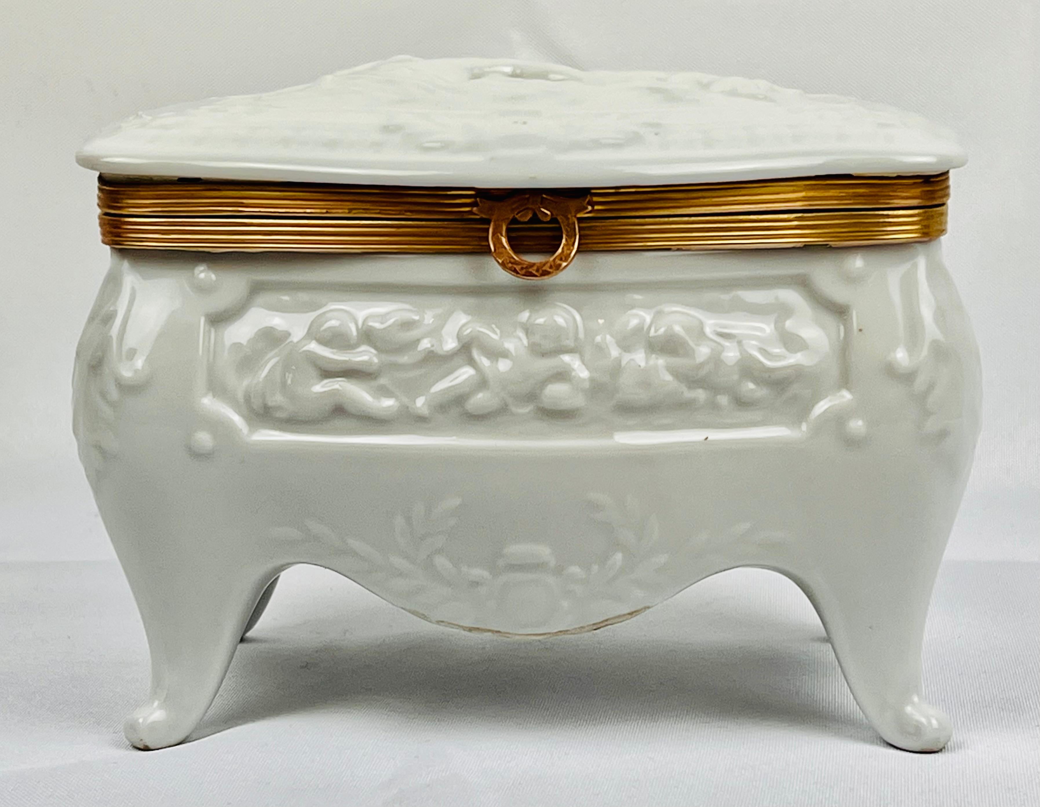 Grande boîte en porcelaine de Paris ancienne à glaçure blanche en forme de commode bombée.  Le panneau supérieur représente une femme nue avec deux chiens.  Le panneau avant est composé de putti qui gambadent.  Le cadre à charnière joliment doré est