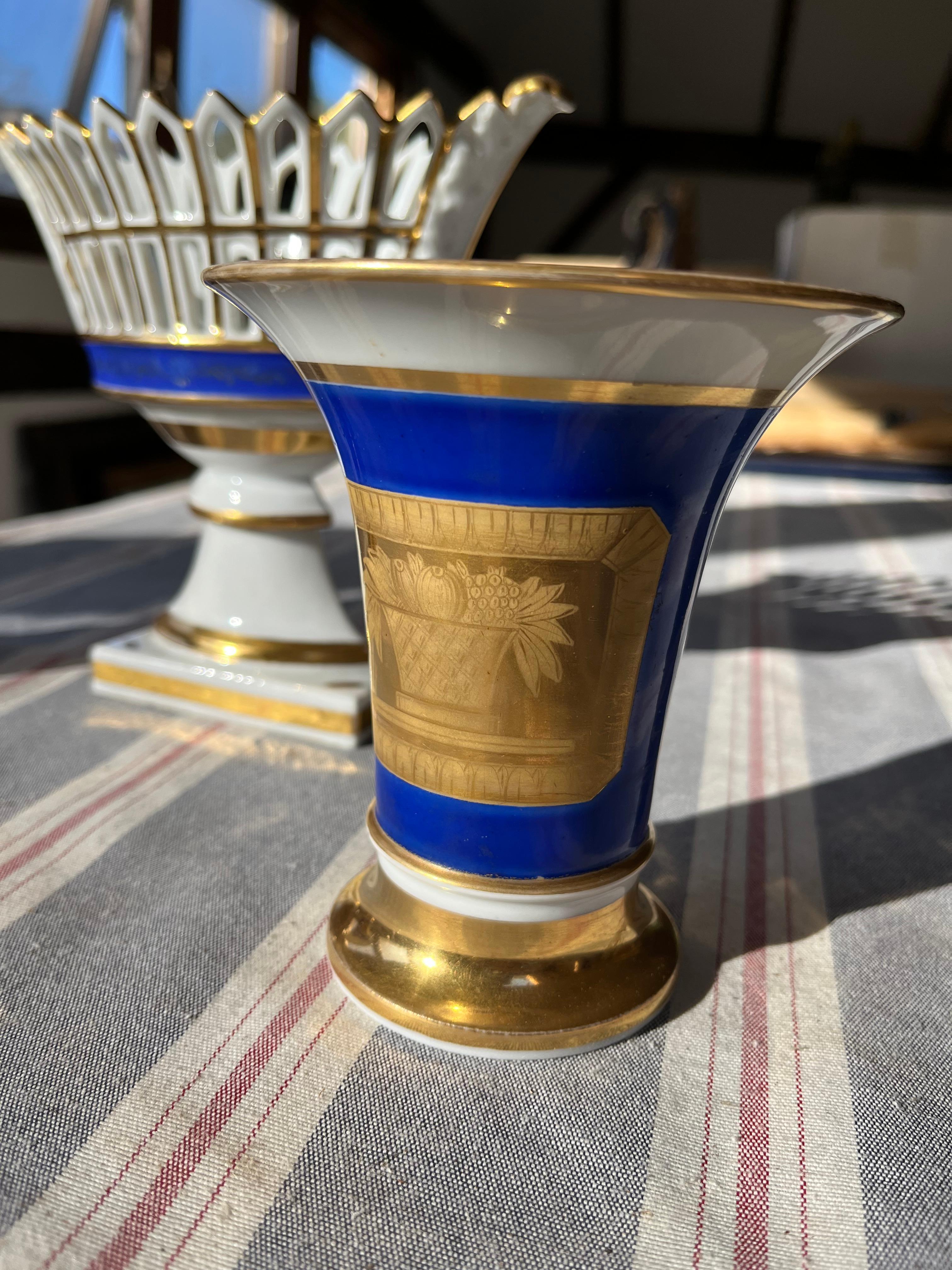 A matched set of Vieux Paris porcelain table articles including a pair of spill vases decorated with embossed gilt decoration, cobalt blue glaze and a hand-painted lyre decoration on the reverse, along with a reticulated potpourri basket, also