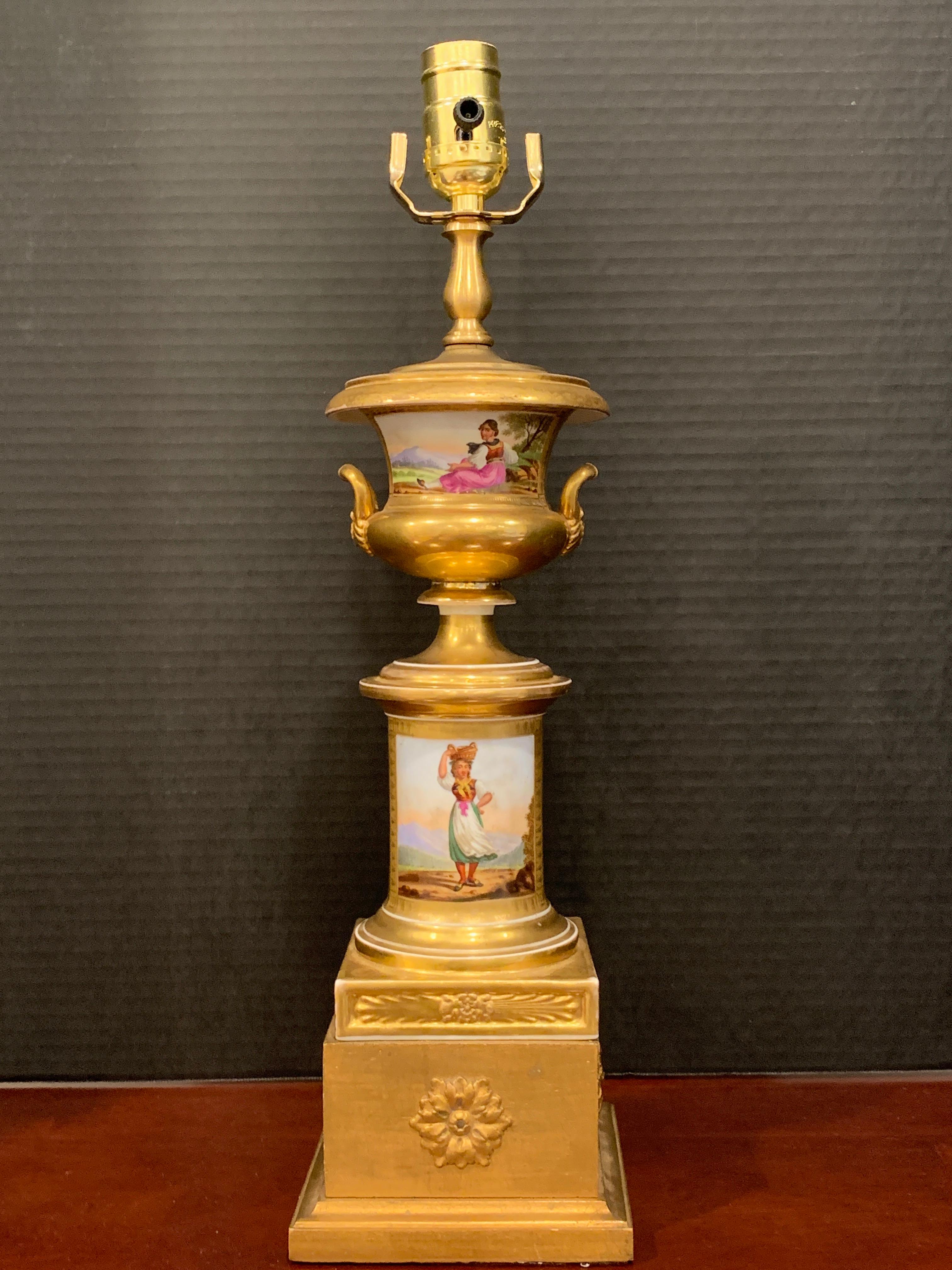 Old Paris Tyrollian fashion motif Campana urn, now as a lamp
The upper part depicting a dressed seated maiden in landscape, the lower section with a standing model with a basket in landscape, with gilt enamel medallions on the back. New