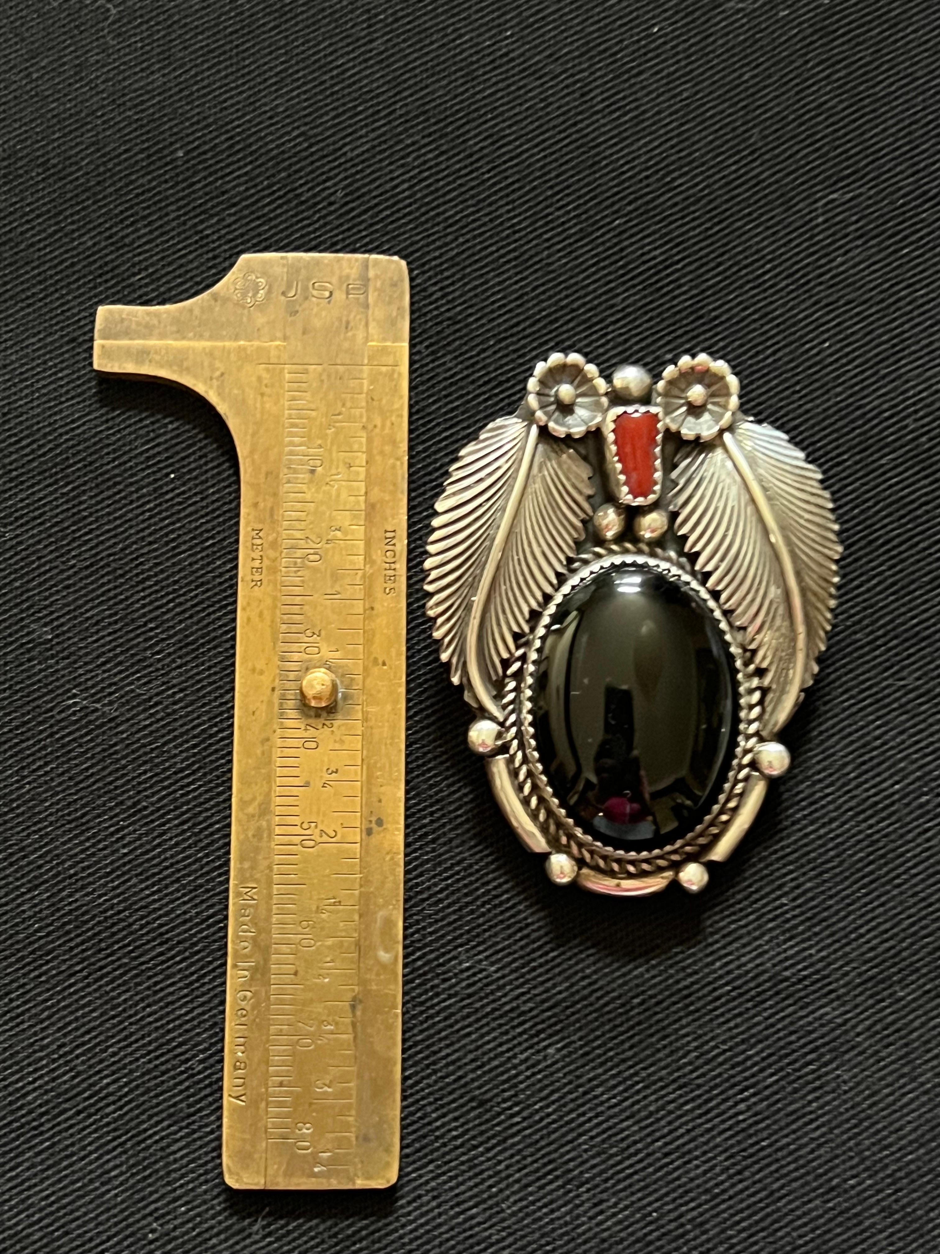 This Bolo owl pendant was handcrafted by Navajo Verdi Jake, marked VJ. The large oval onyx body has huge silver feathers, genuine red coral for the nose, and sterling flowers for the eyes. The body has a v- notched bezel surrounded by heavy twisted