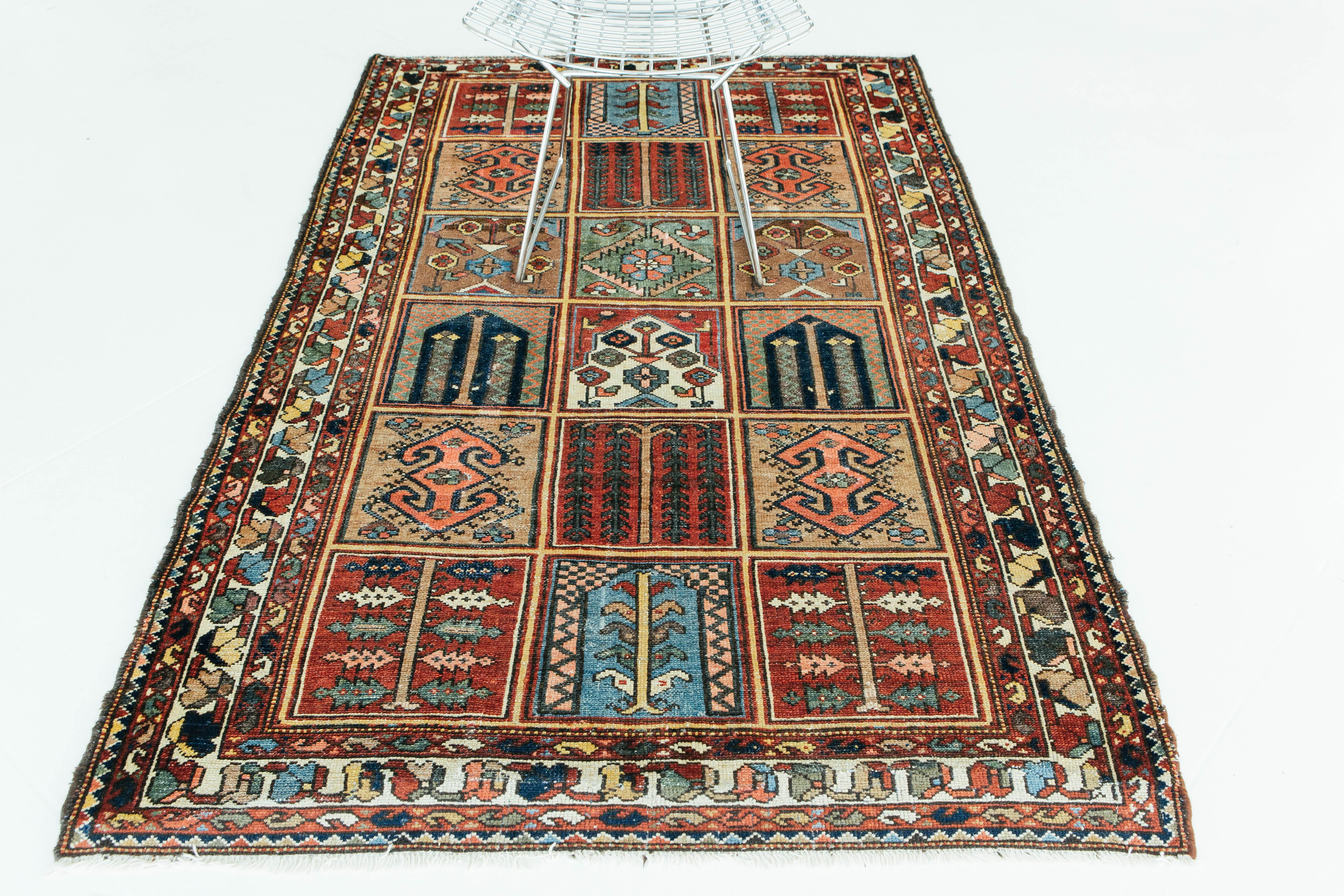 An antique Bakhtiari Garden Design rug woven in the Zagros Mountains of Iran. This garden design rug uses vibrant colors to create square compartments filled with floral motives, such as a willow tree, a grapevine, or a vase. This piece is both