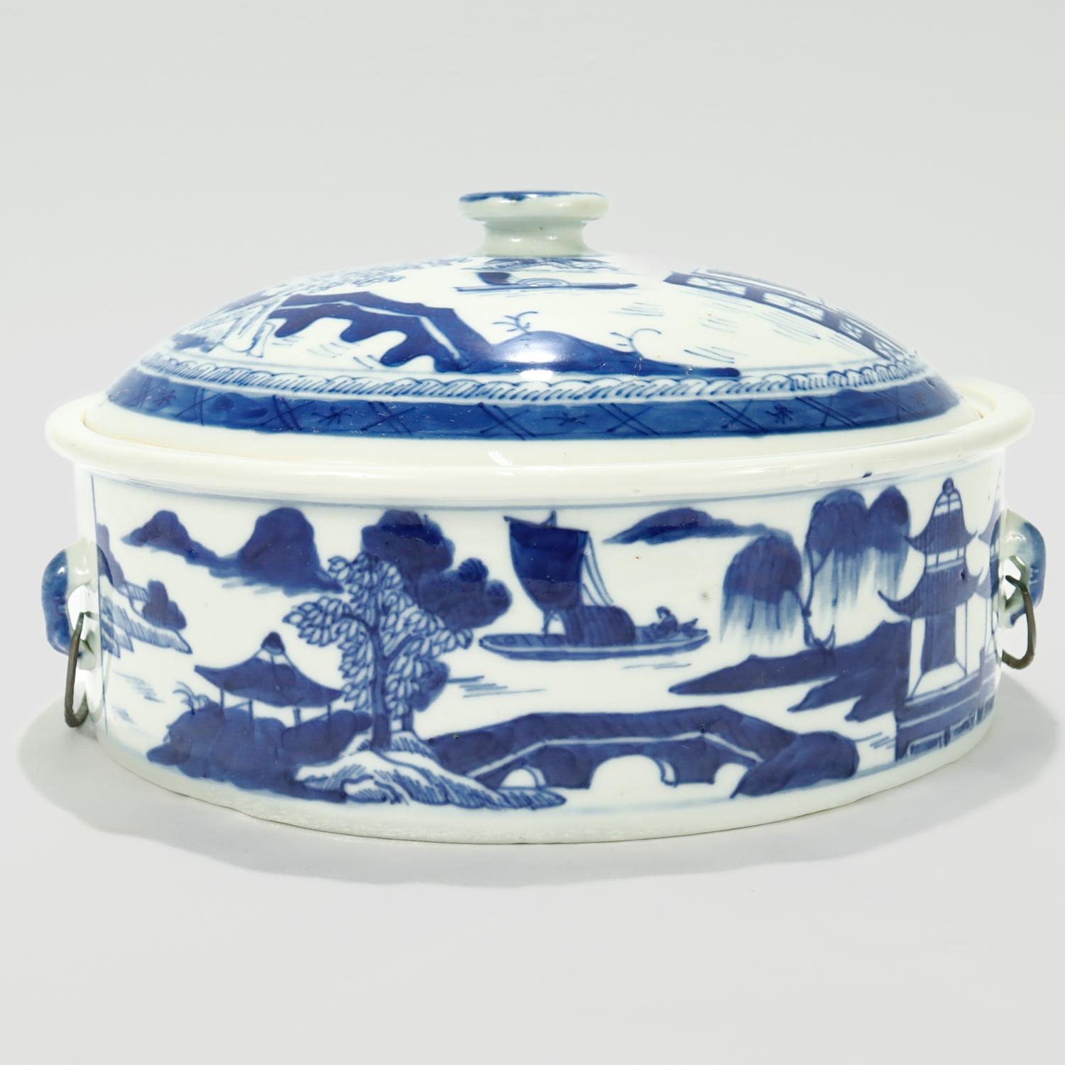 A fine antique Chinese export porcelain covered tureen or vegetable dish.

In the Canton pattern.

Decorated in underglaze blue.

Depicting a mountainous Chinese village to the top of the lid and the long sides of the body. The background has
