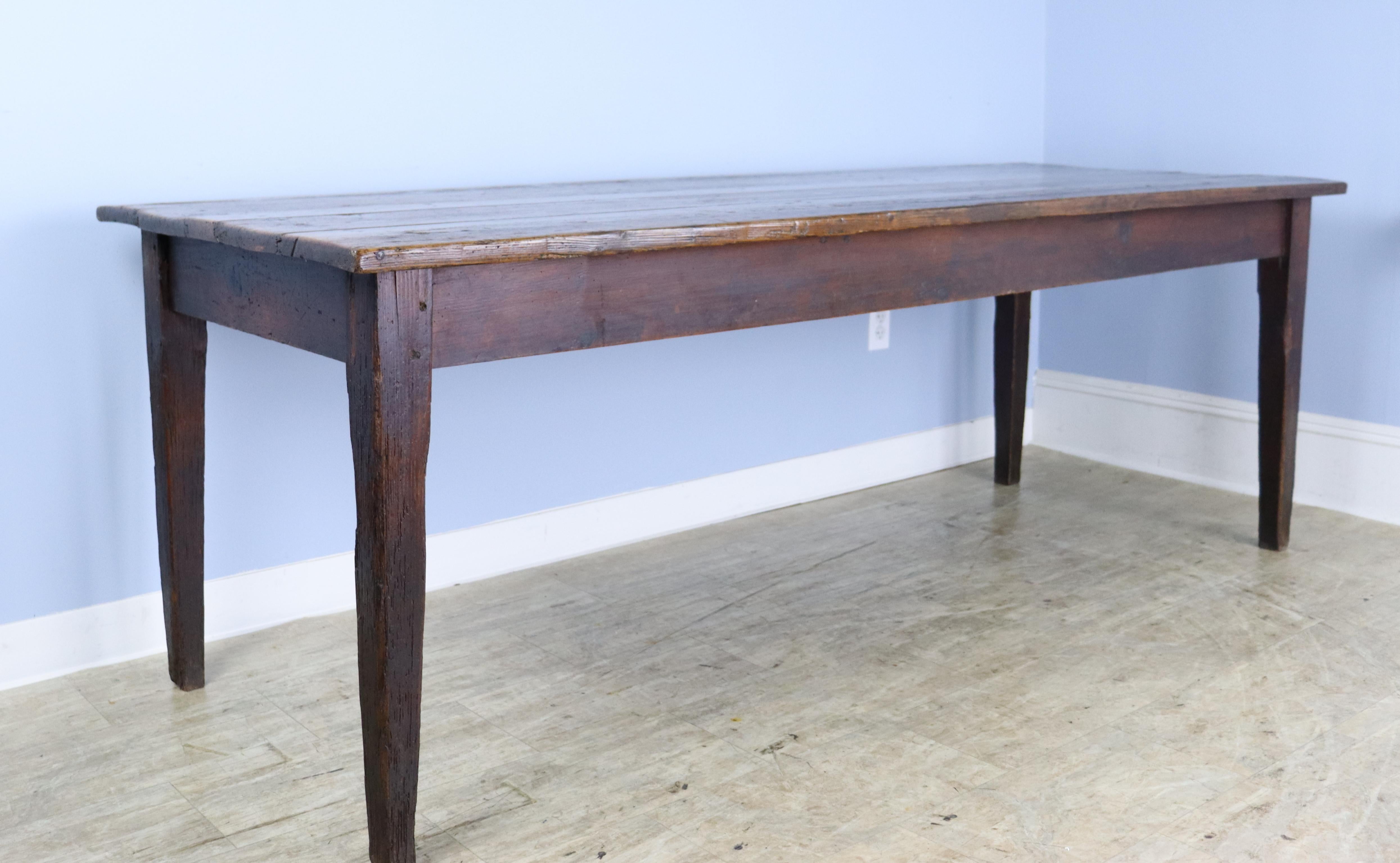 A classic pine farm table, generously proportioned with unusually good depth for a table of this age. Nice tapered legs and mellow color. The top and legs have dramatic original distress which adds a strong note of interest, shown in several of the