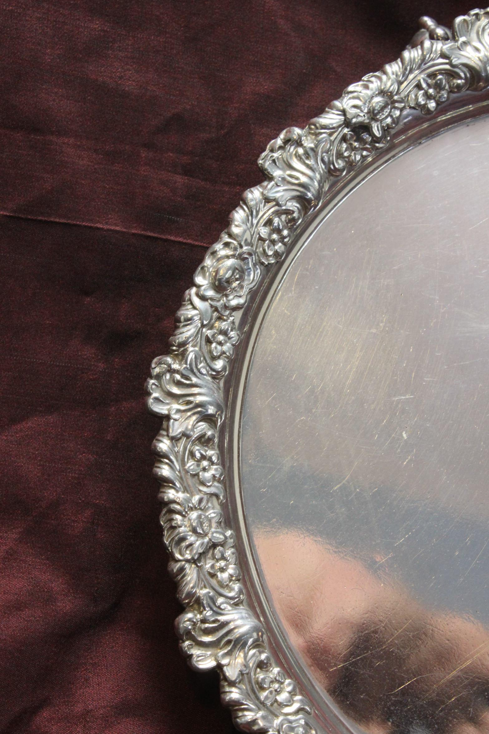 This Old Sheffield Plate card tray measures 220 mm (8.75 inches) in diameter and stands 30 mm (1.25 inches) high. The edge of the tray which is decorated profusely with flowers and flourishes, is made up of sections of stamped silver which have been