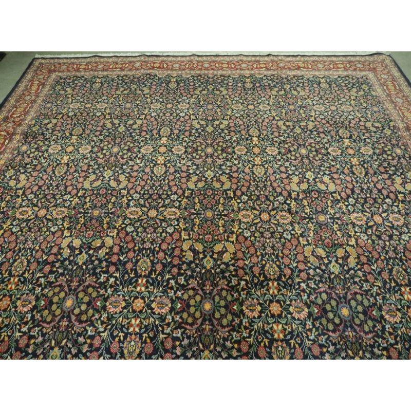 Der Teppich ist wunderschön gezeichnet mit einem allover 'mille fleur'-Muster auf indigoblauem Hintergrund. Die Blumen sind in sanften Pastellfarben gehalten, die dem Teppich einen leichten Charakter verleihen. Die detaillierte Bordüre auf rotem