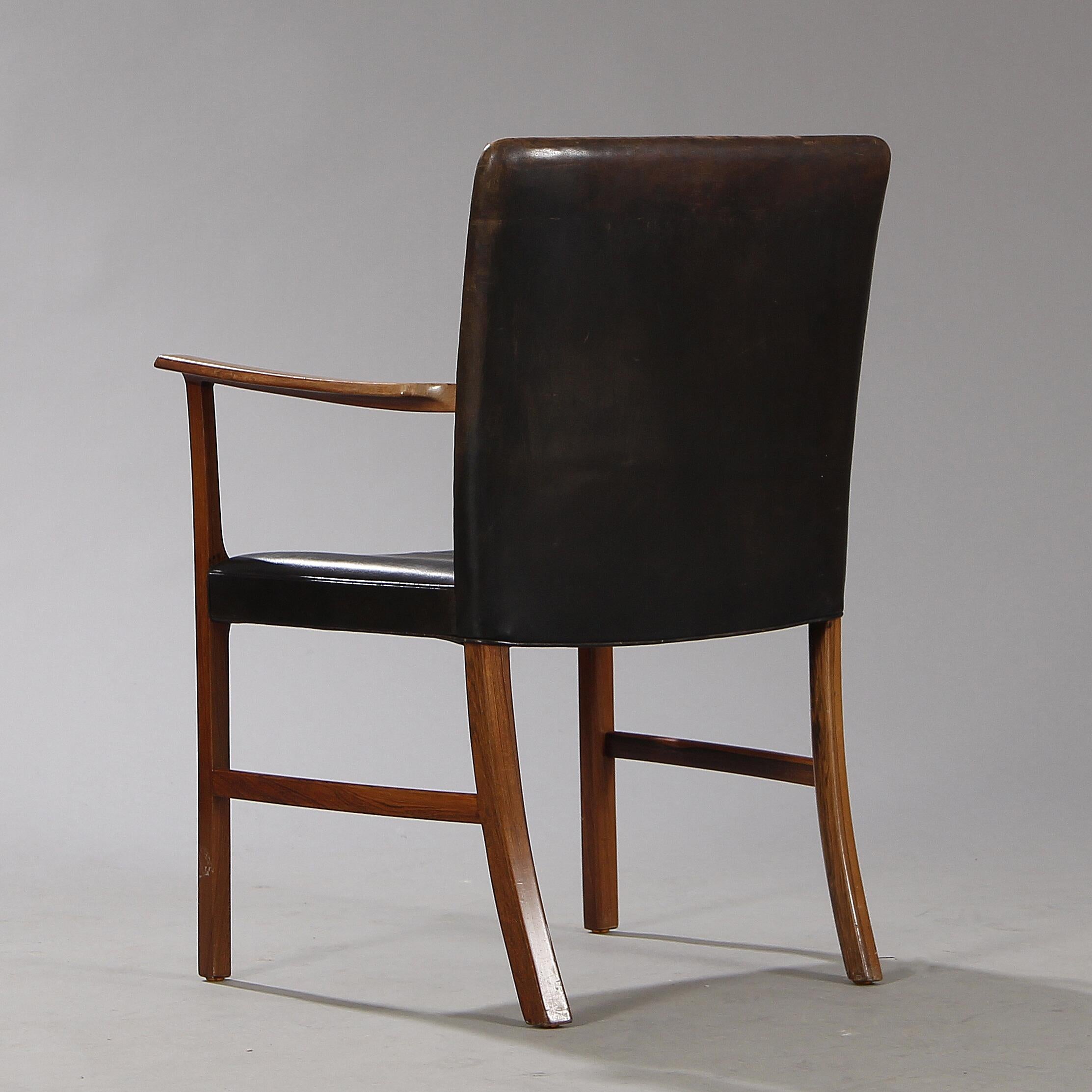 Armchair with rosewood frame by Ole Wanscher. Seat and back upholstered with black leather. Made by cabinetmaker A. J. Iversen.

Normal patina due to age and use including scratches and marks. 
Seat with repair, as pictured.