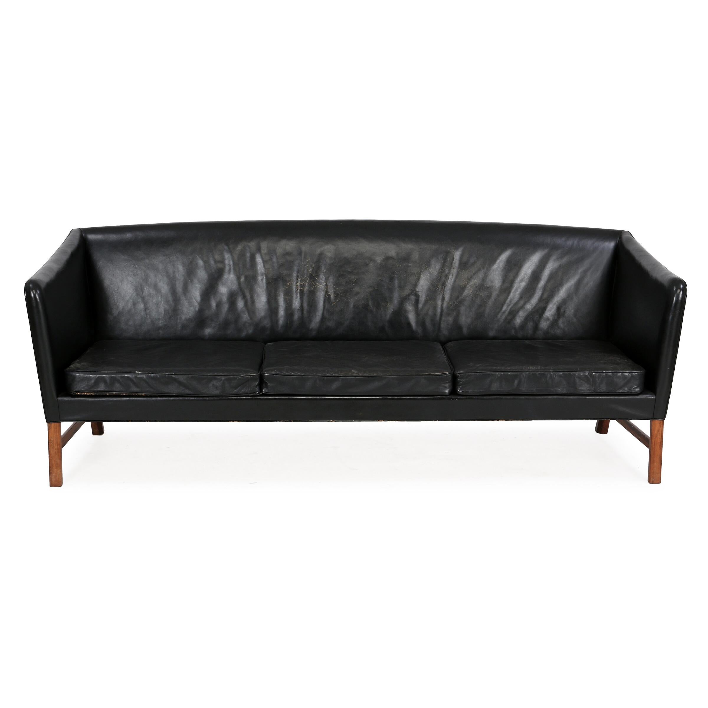 Freestanding three seater sofa with Brazilian rosewood frame by Ole Wanscher. Seat, sides and back upholstered with black leather. Made by cabinetmaker A. J. Iversen.

Fair condition with some crackling of leather but no structural issues.
